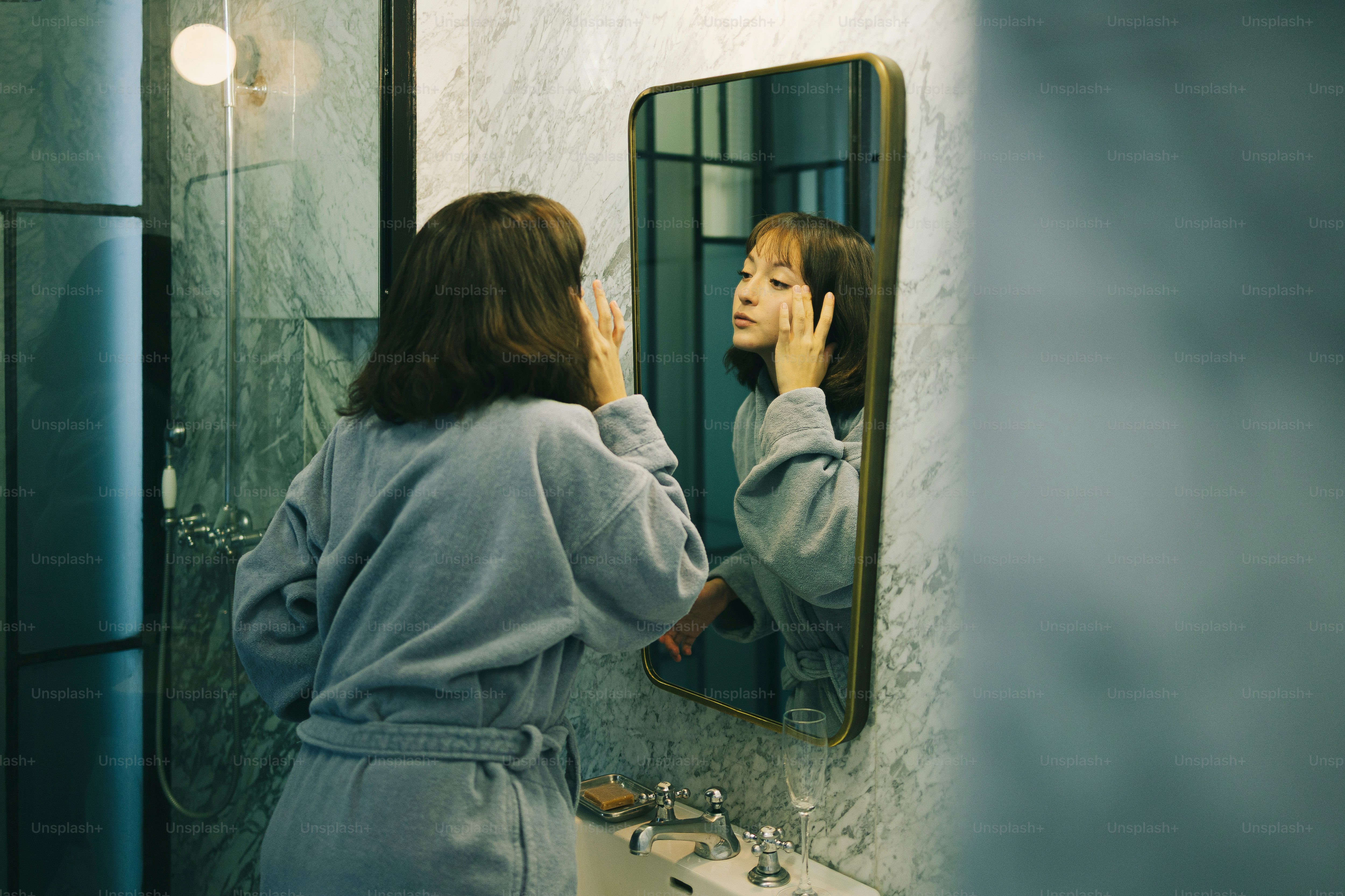 Woman examines her face in a bathroom mirror.
