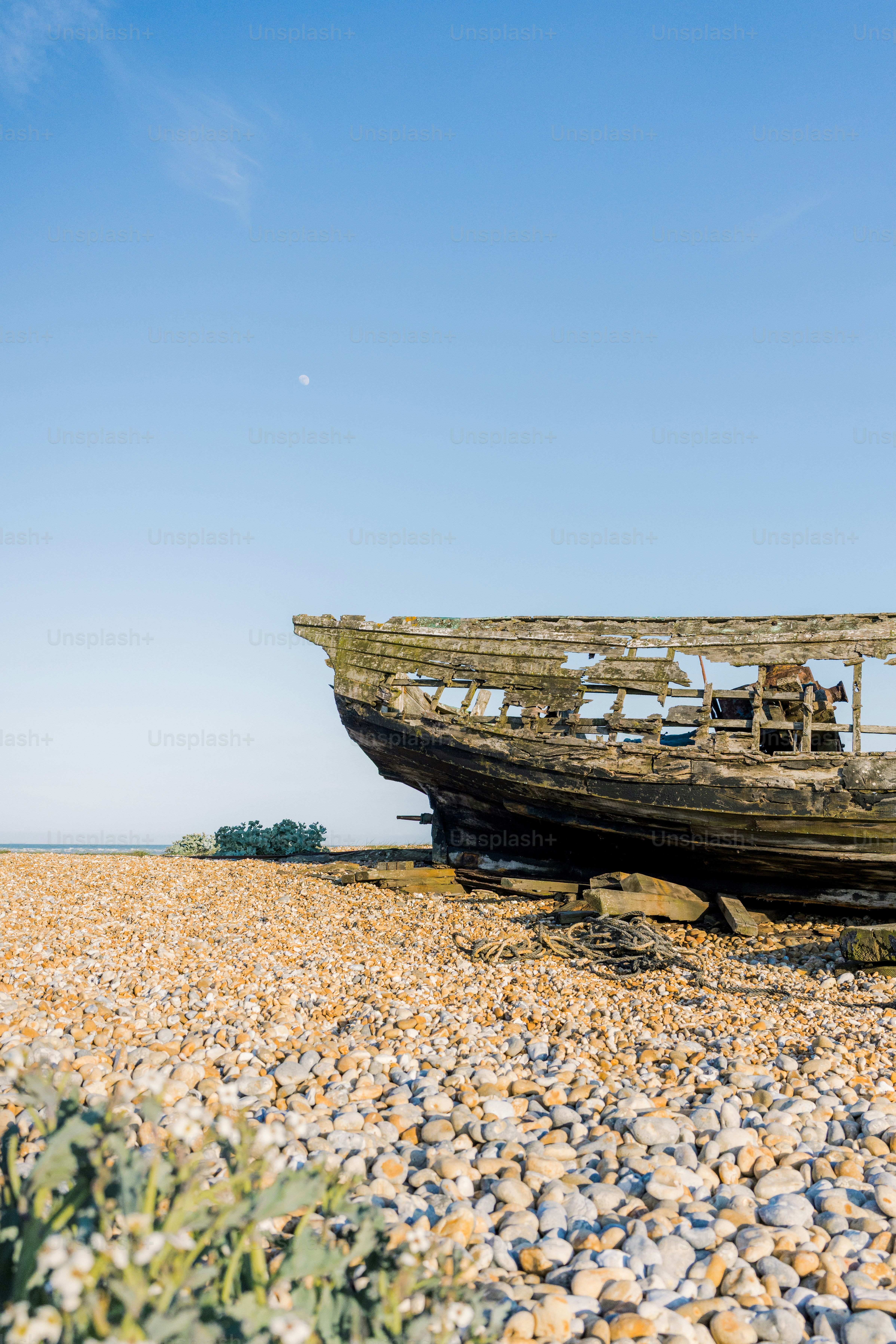 A weathered boat rests on a pebble beach.