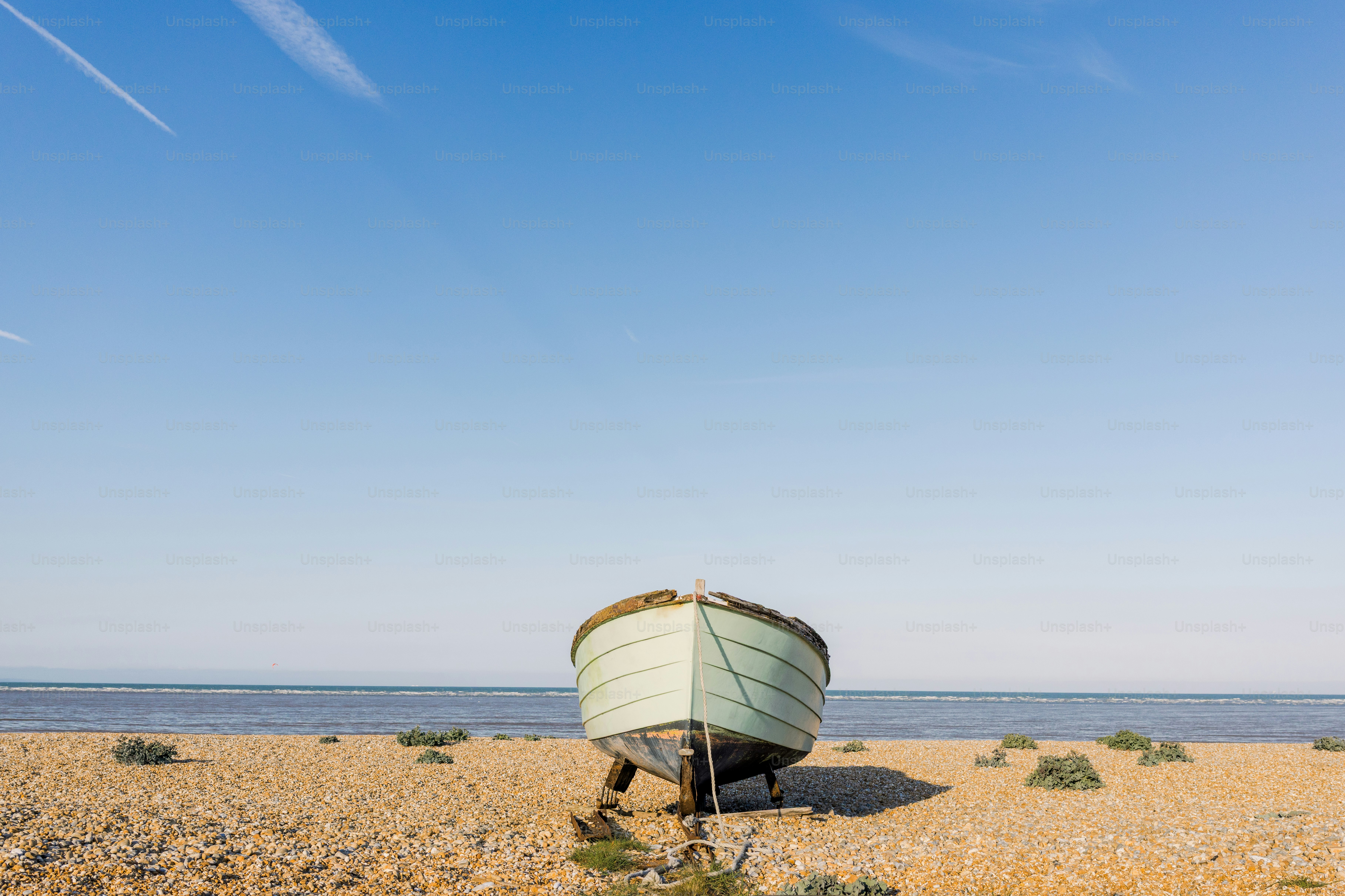A boat sits on a sandy beach under a blue sky.