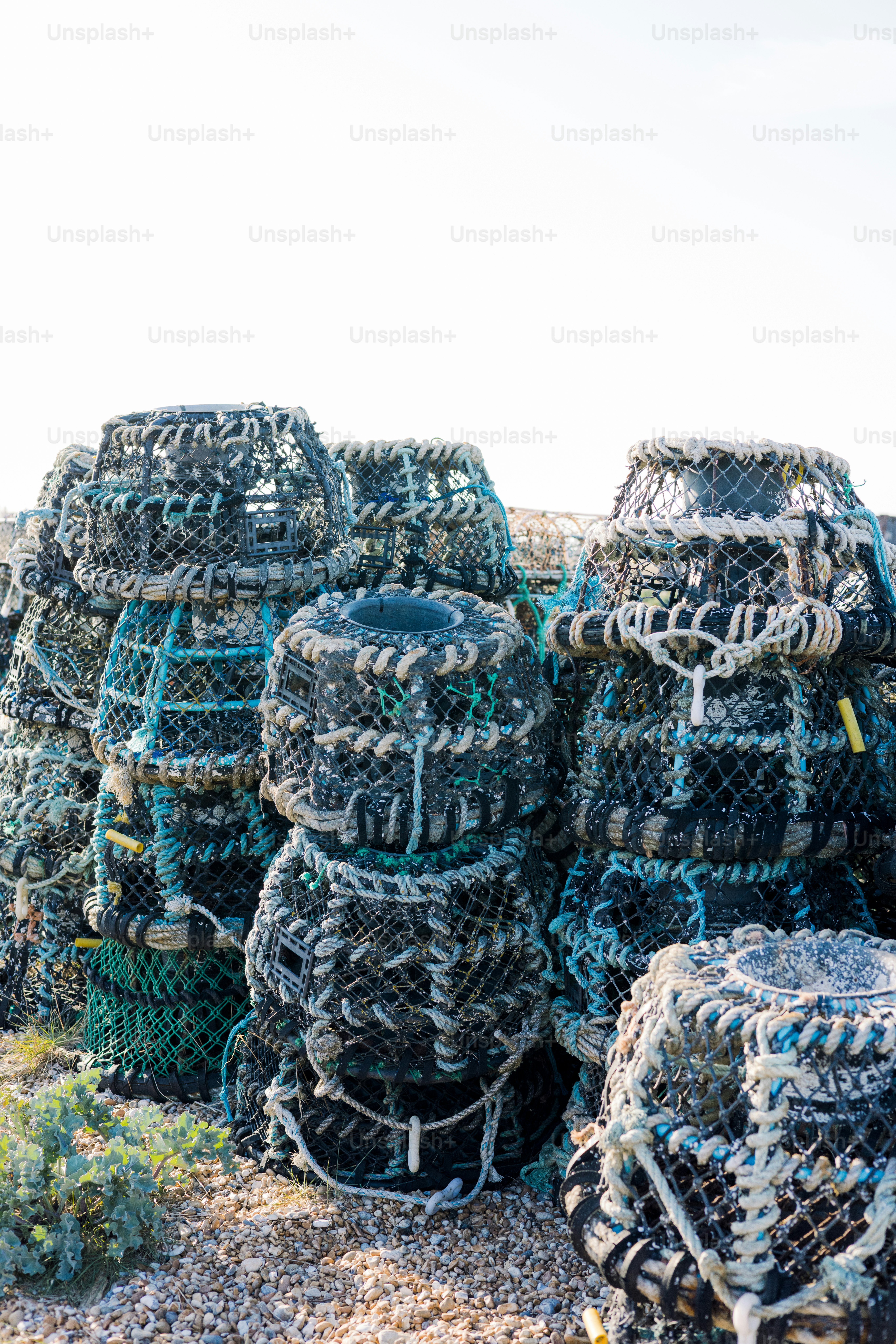 Lobster traps are stacked on a sunny beach.