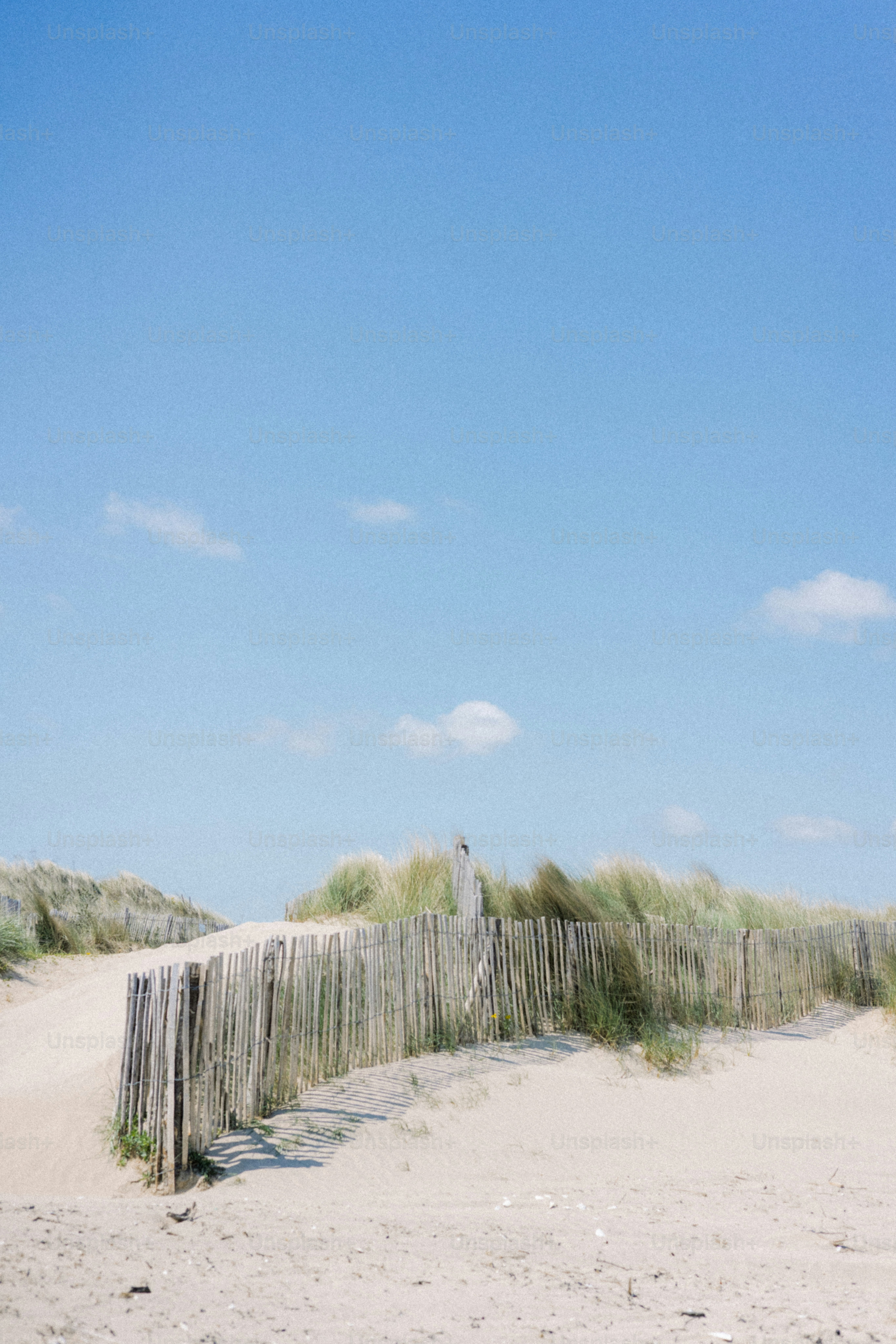 Sandy dunes and fence under a blue sky.