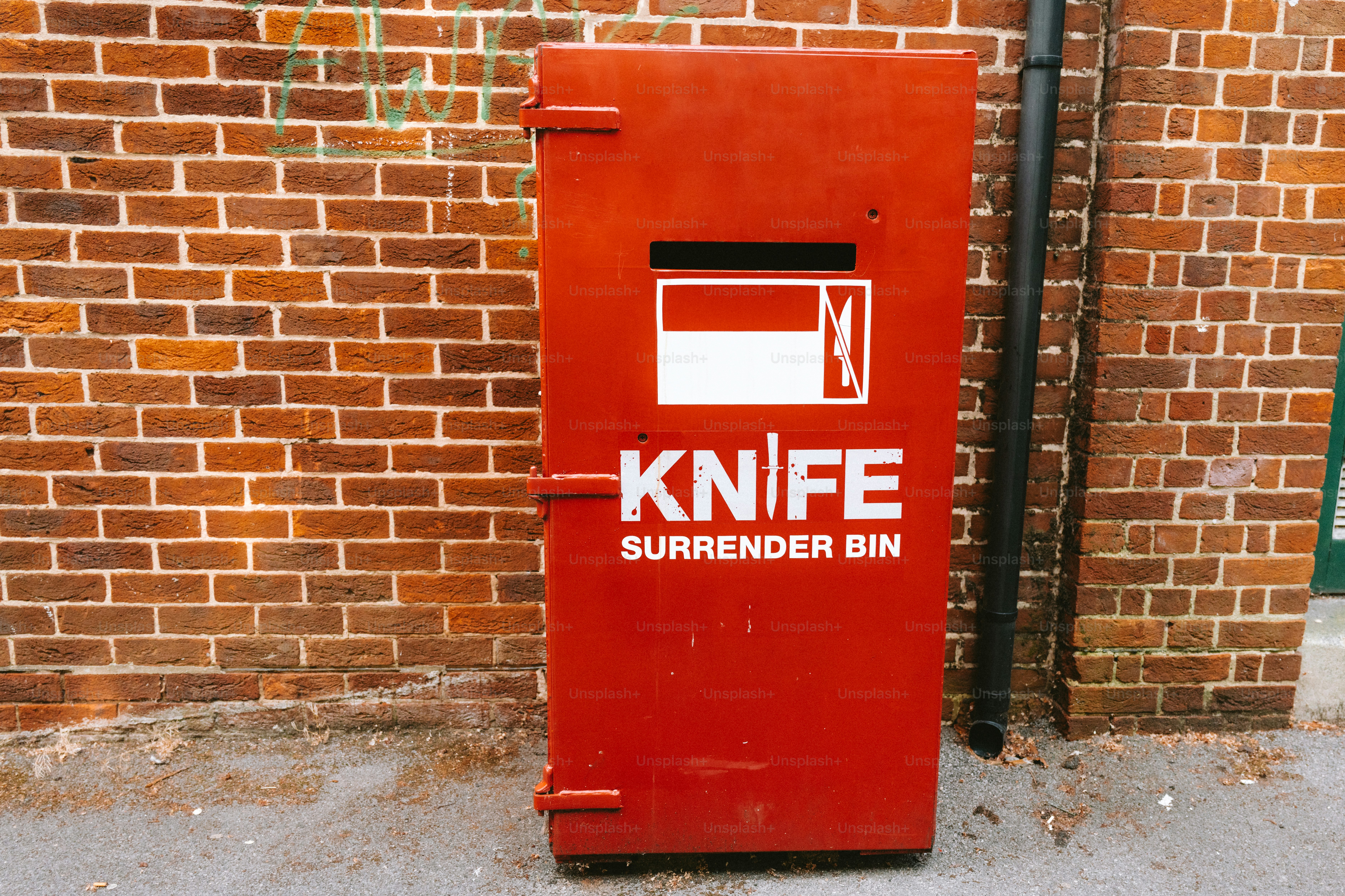 Red knife surrender bin beside a brick wall.