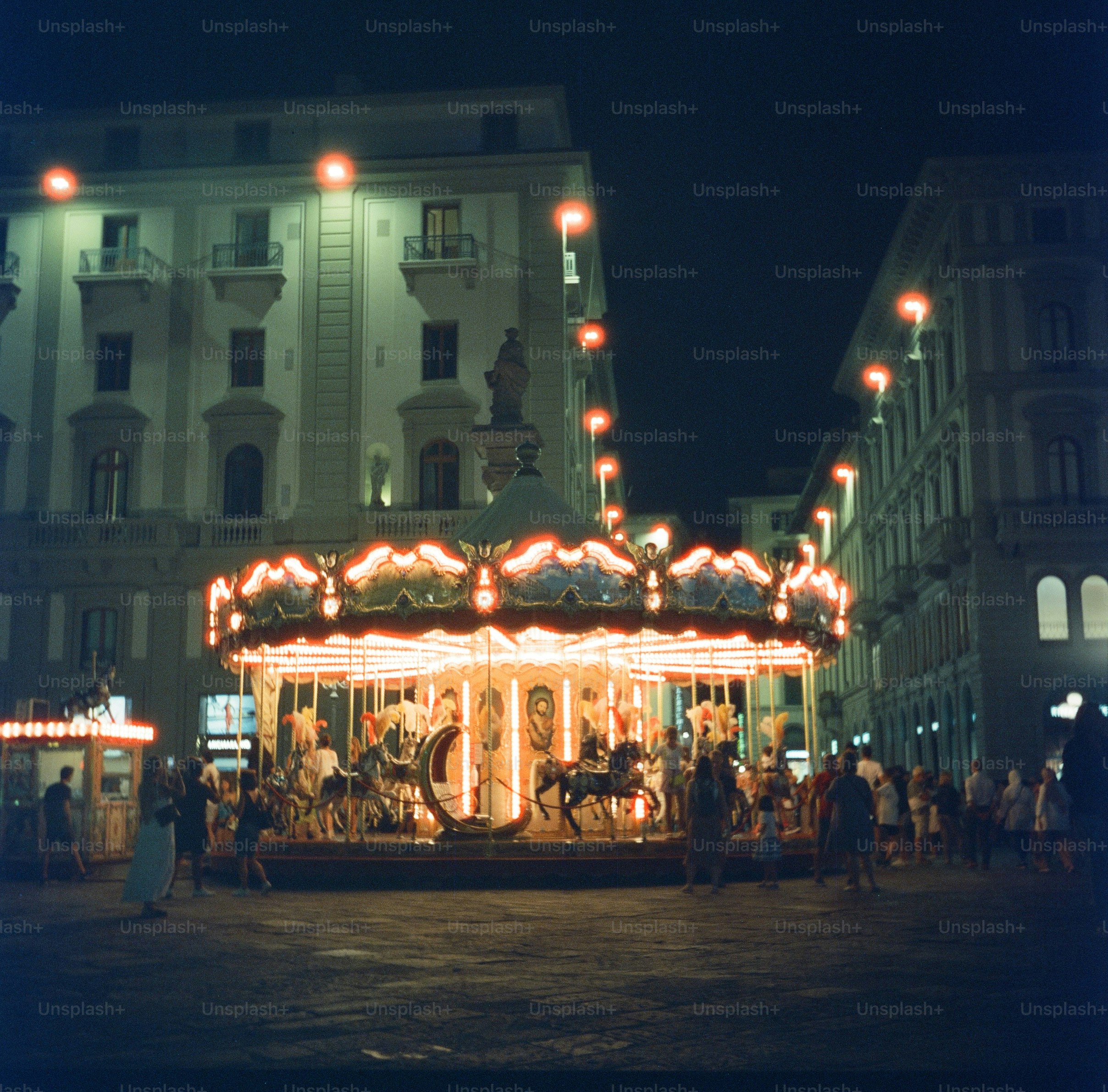 A lit-up carousel in a city square at night.