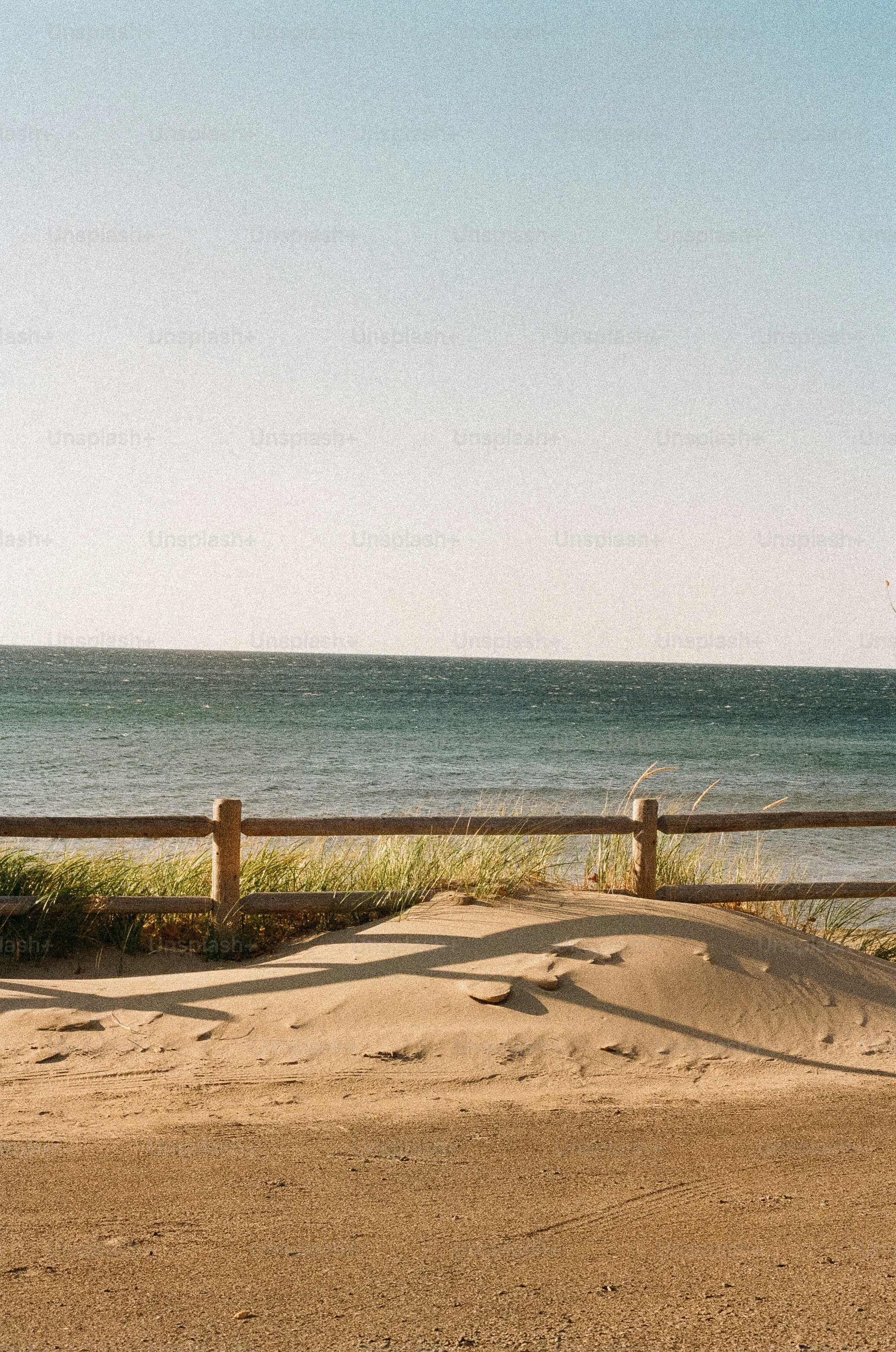 A sandy beach with a wooden fence and ocean.