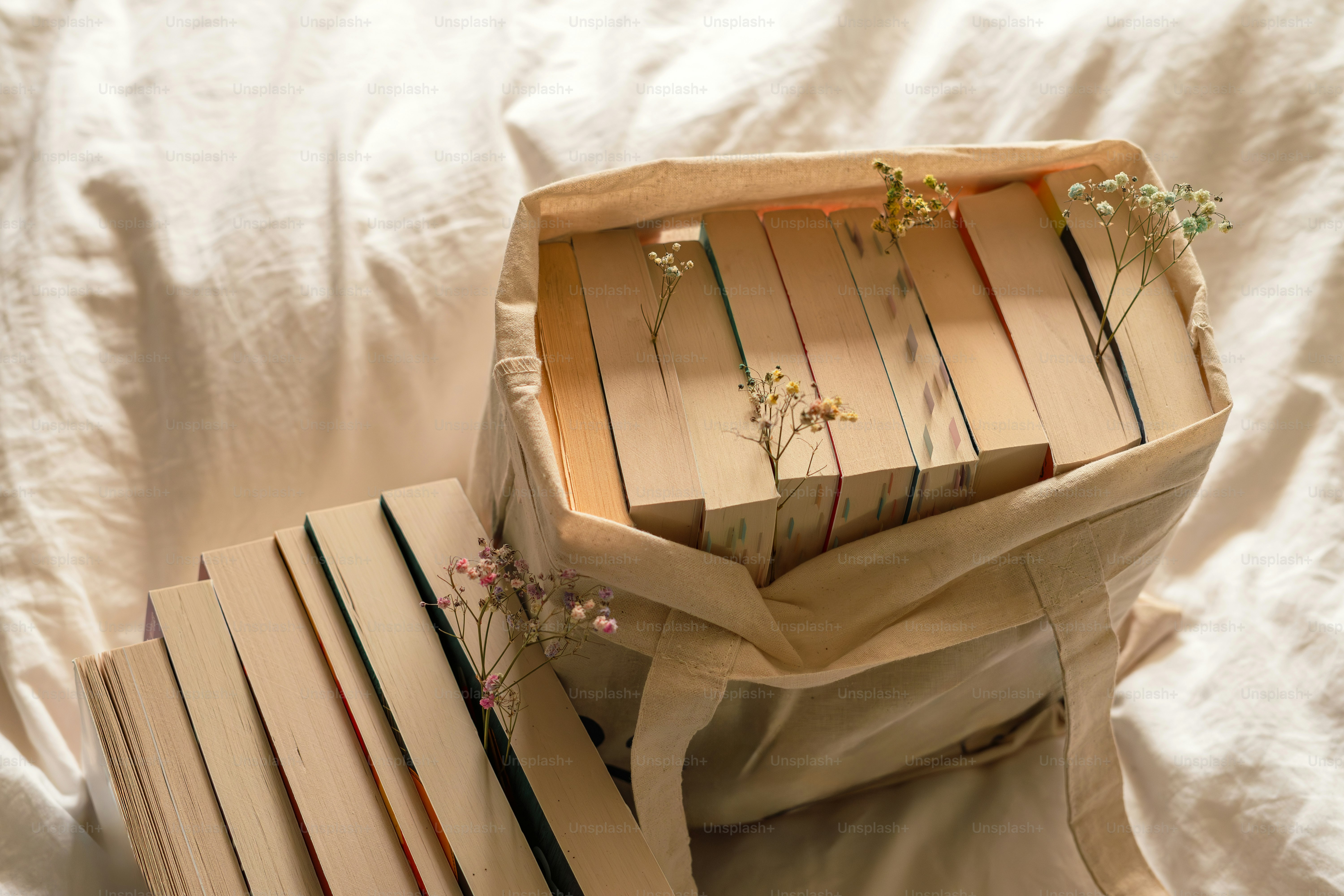 Books in a tote bag, with flowers beside them.