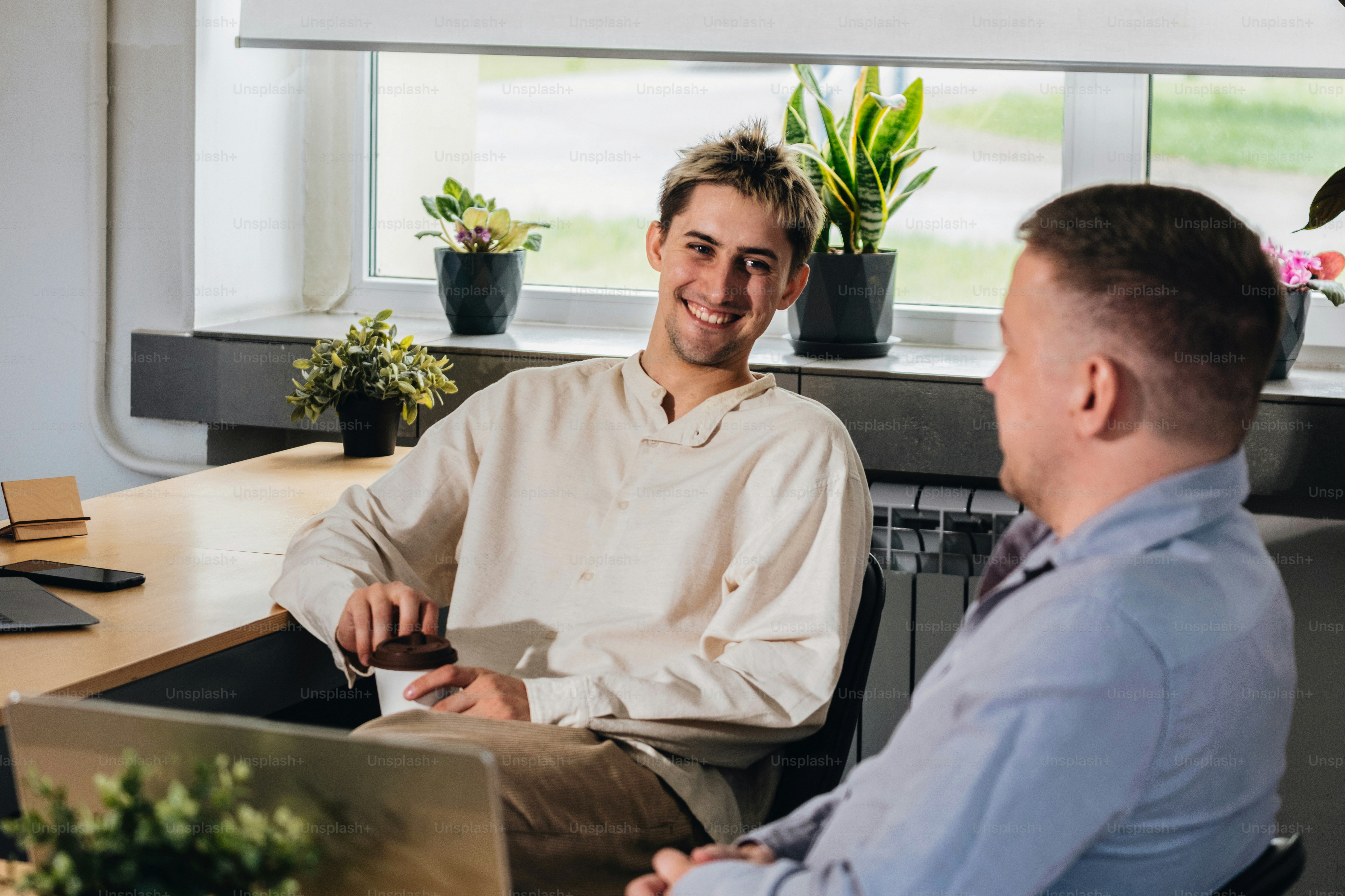 Two men smile and chat in a bright office space.