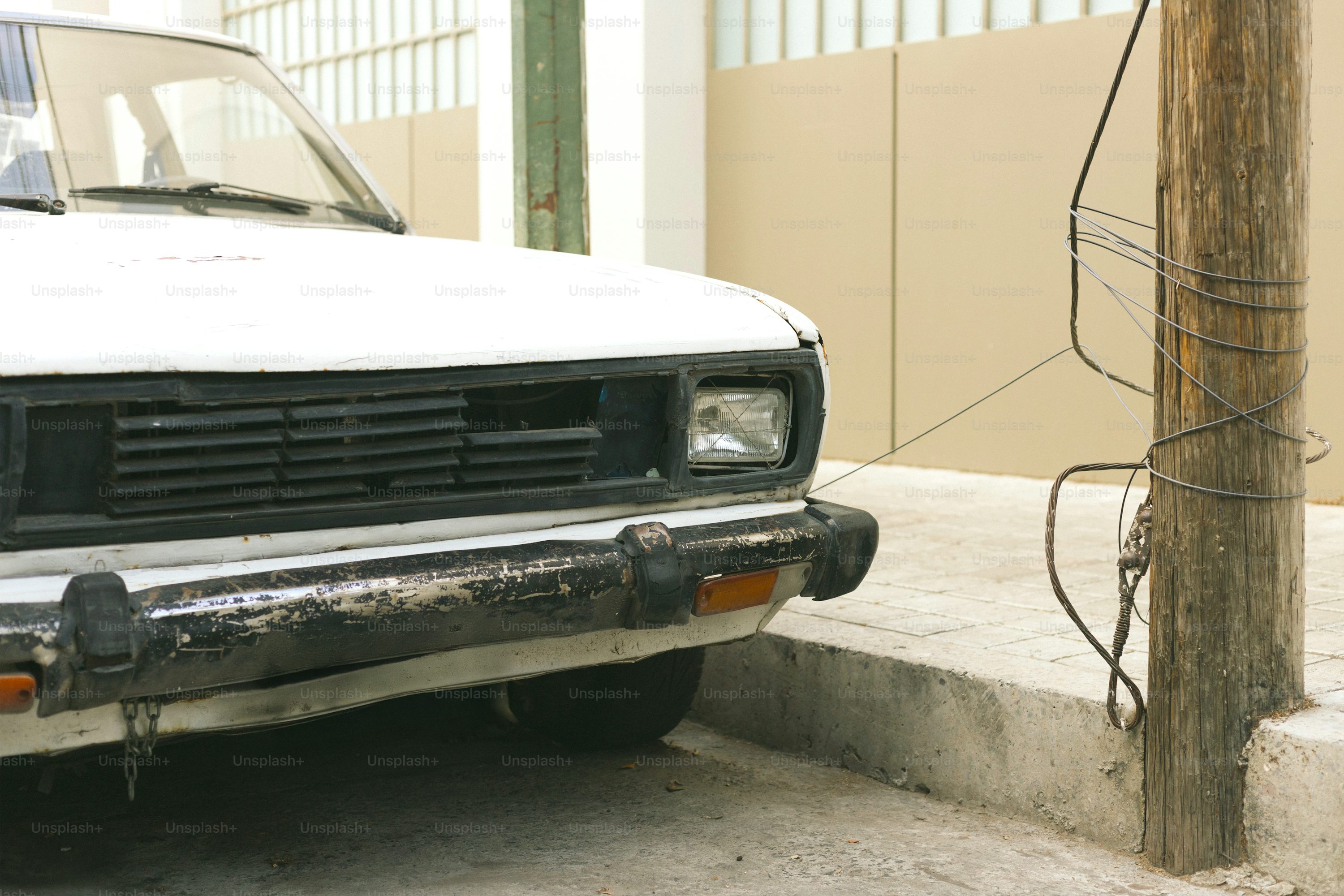 A white car is parked next to a wooden pole.