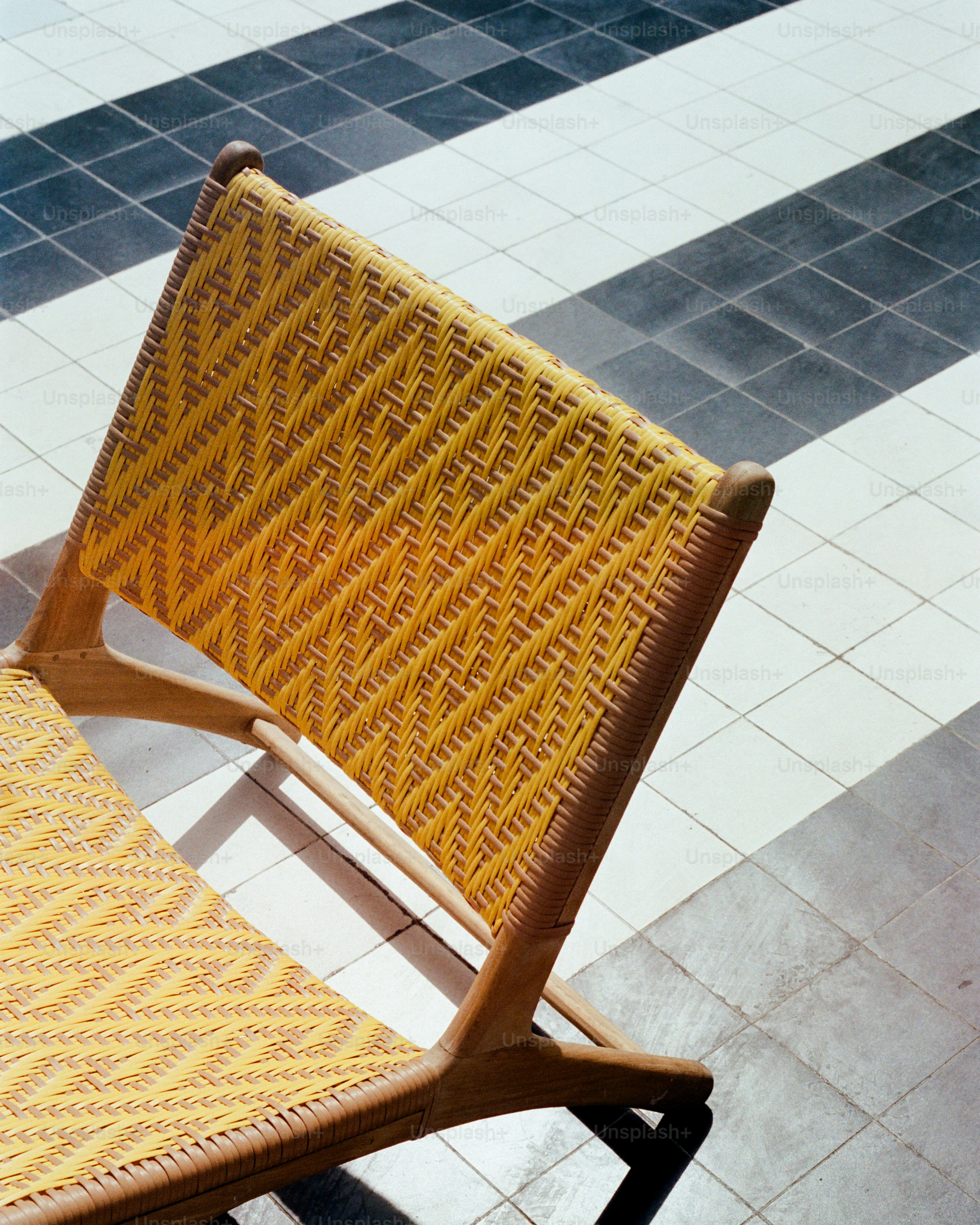 A yellow woven chair sits on a black and white floor.