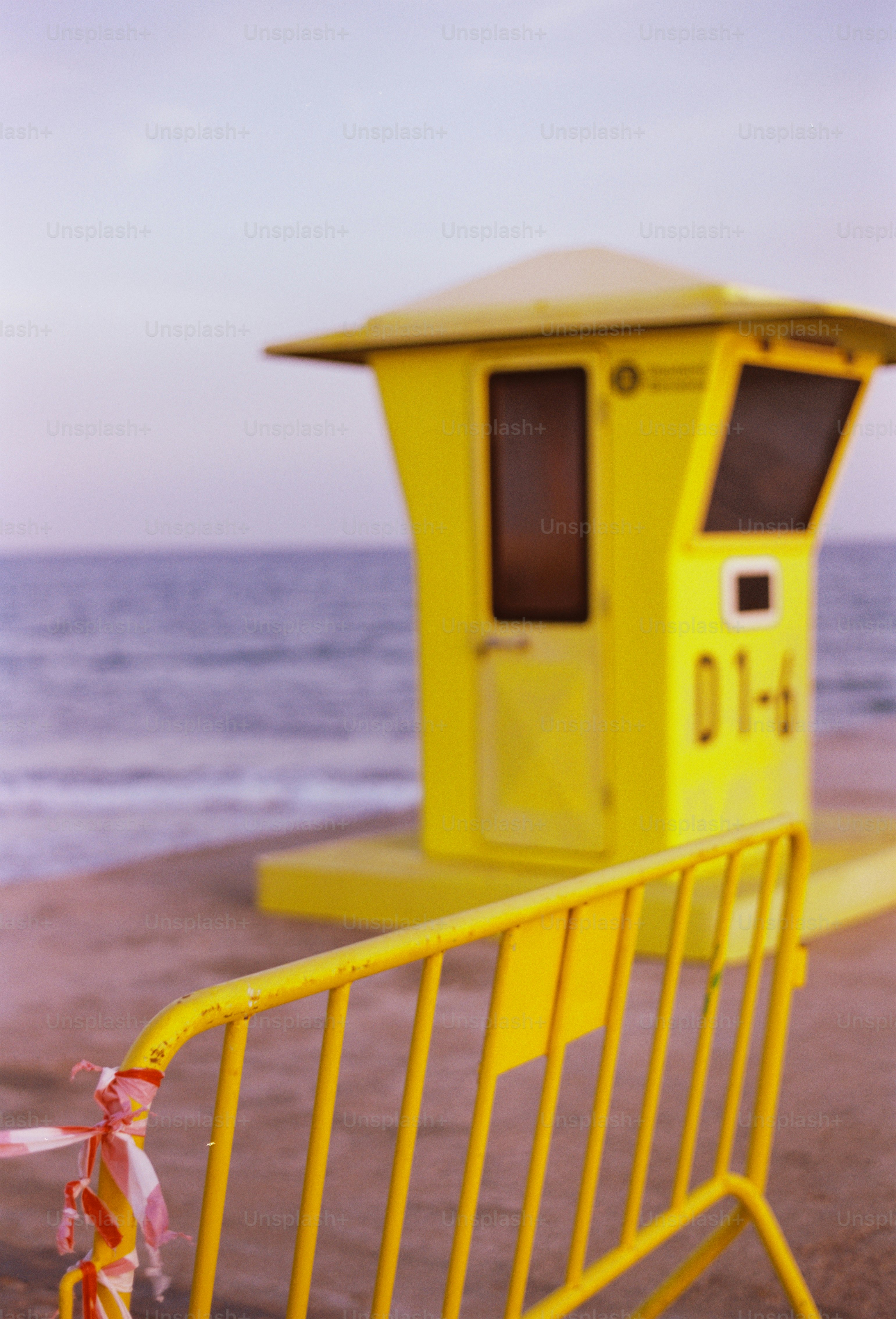 A bright yellow lifeguard station stands near the ocean. photo – Film ...