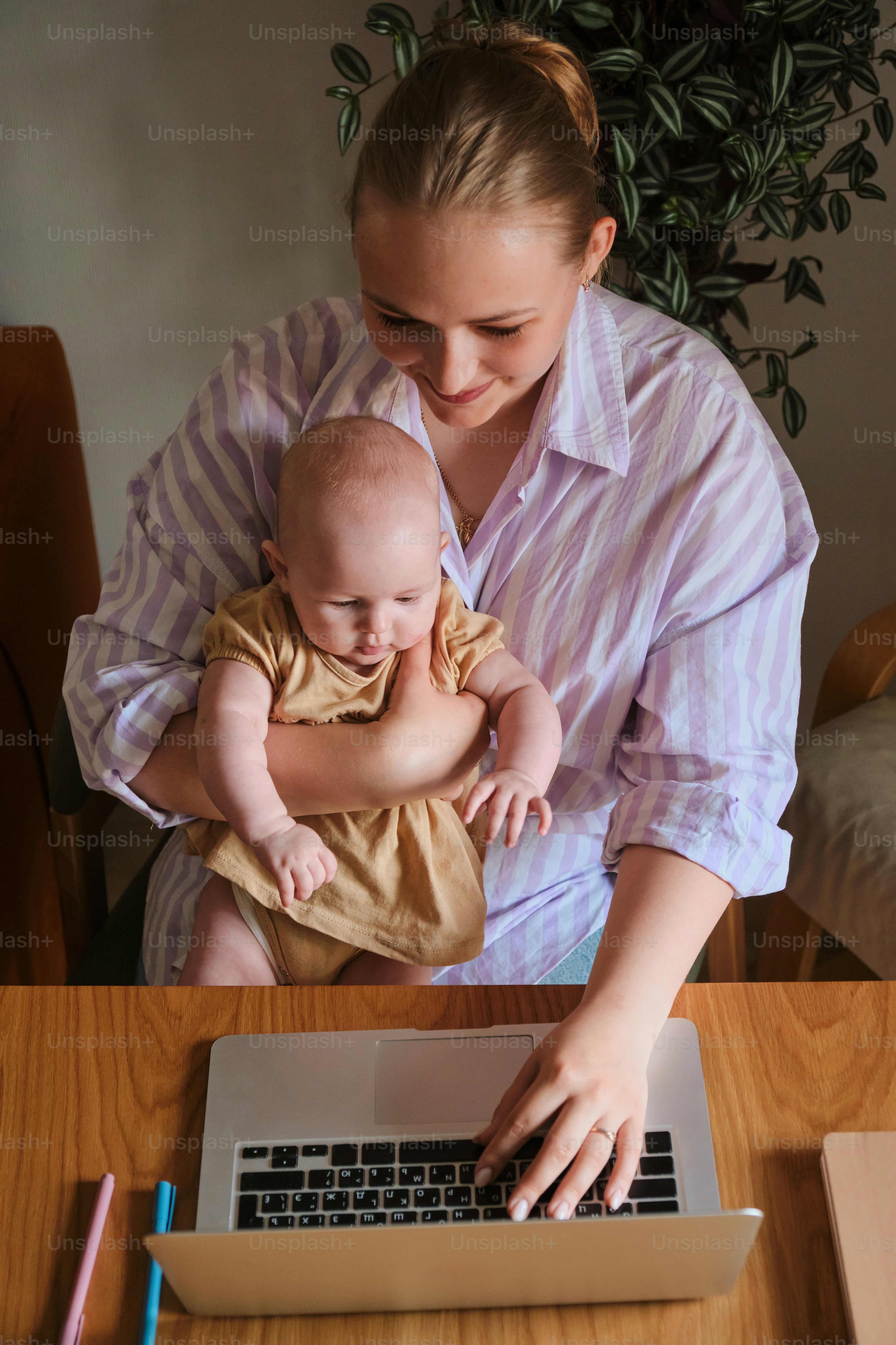 Mamá trabaja en la computadora portátil mientras sostiene a su bebé ...