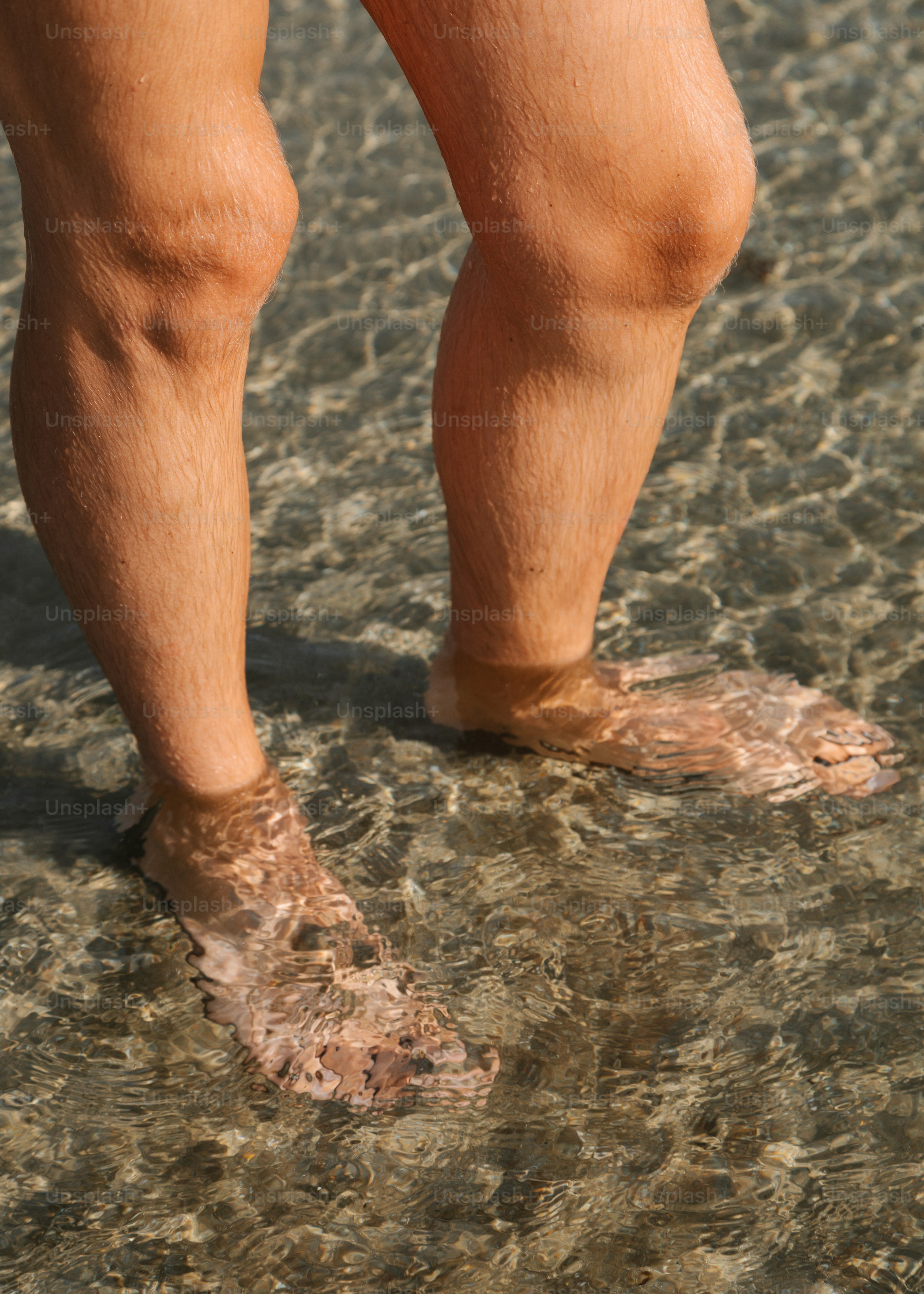 Legs and feet stand in shallow, clear water.