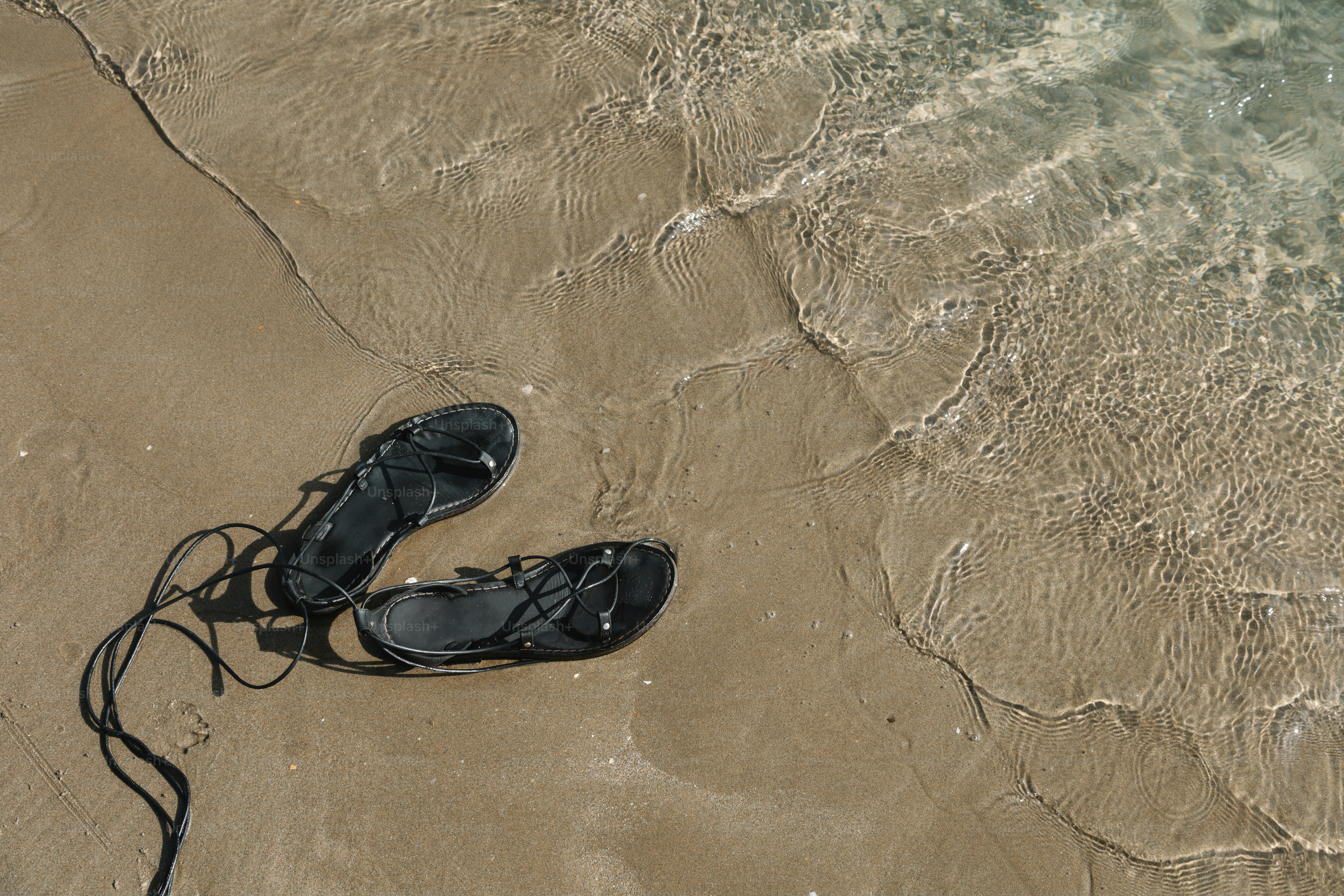 Sandals rest on the shore beside the water.