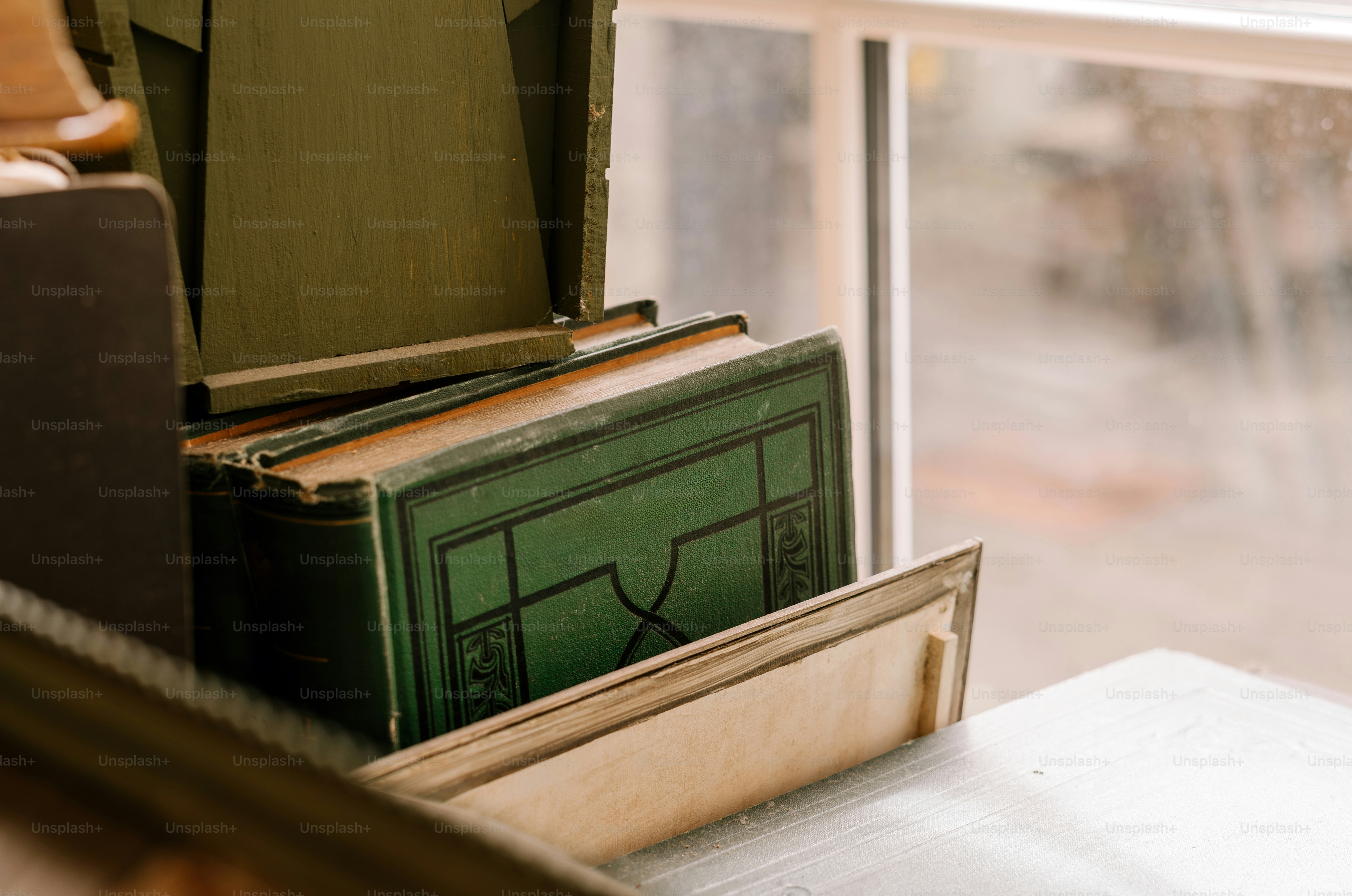Old books are stacked by a window.