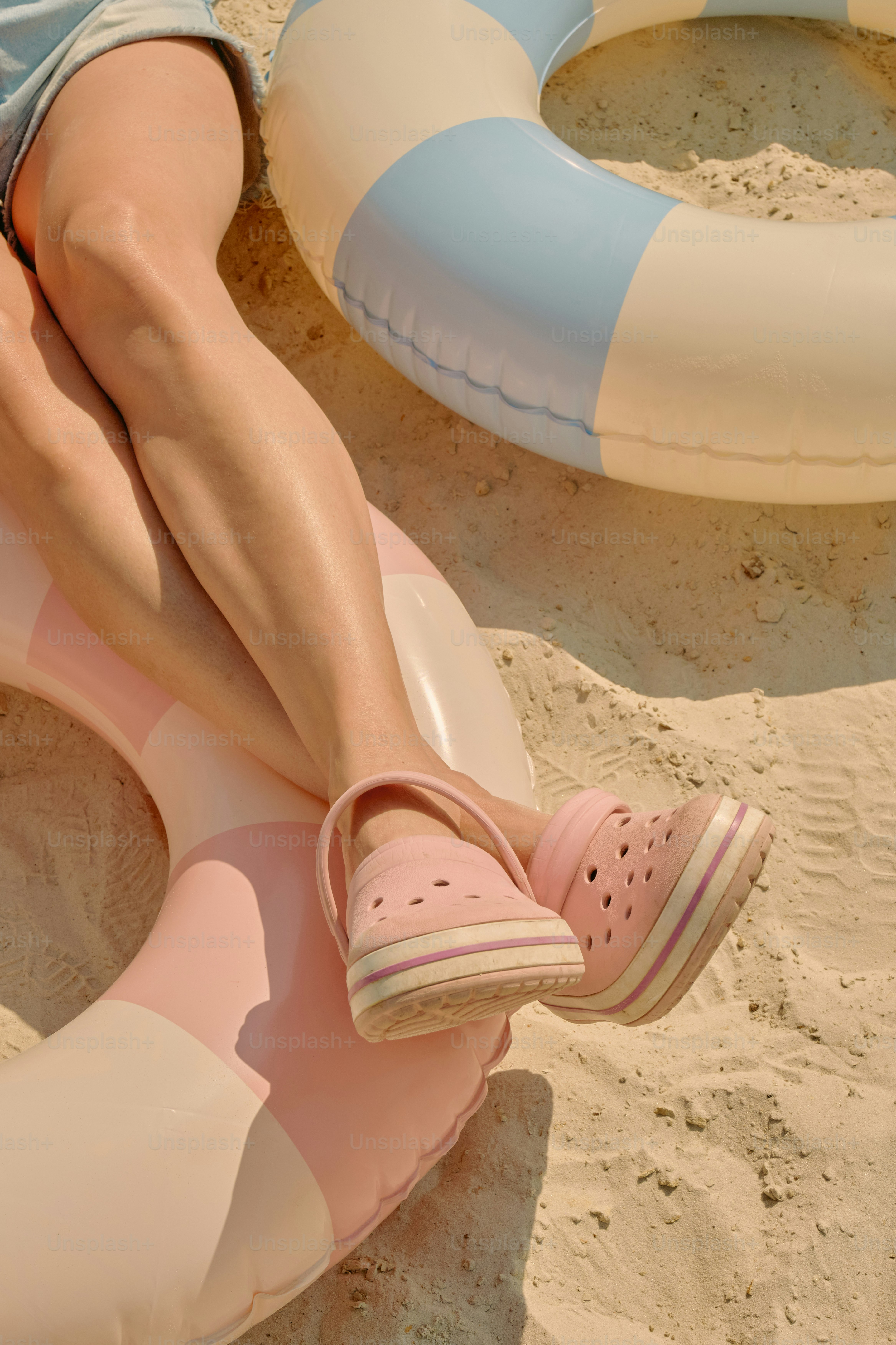 Legs and feet relax near a floatie at the beach.