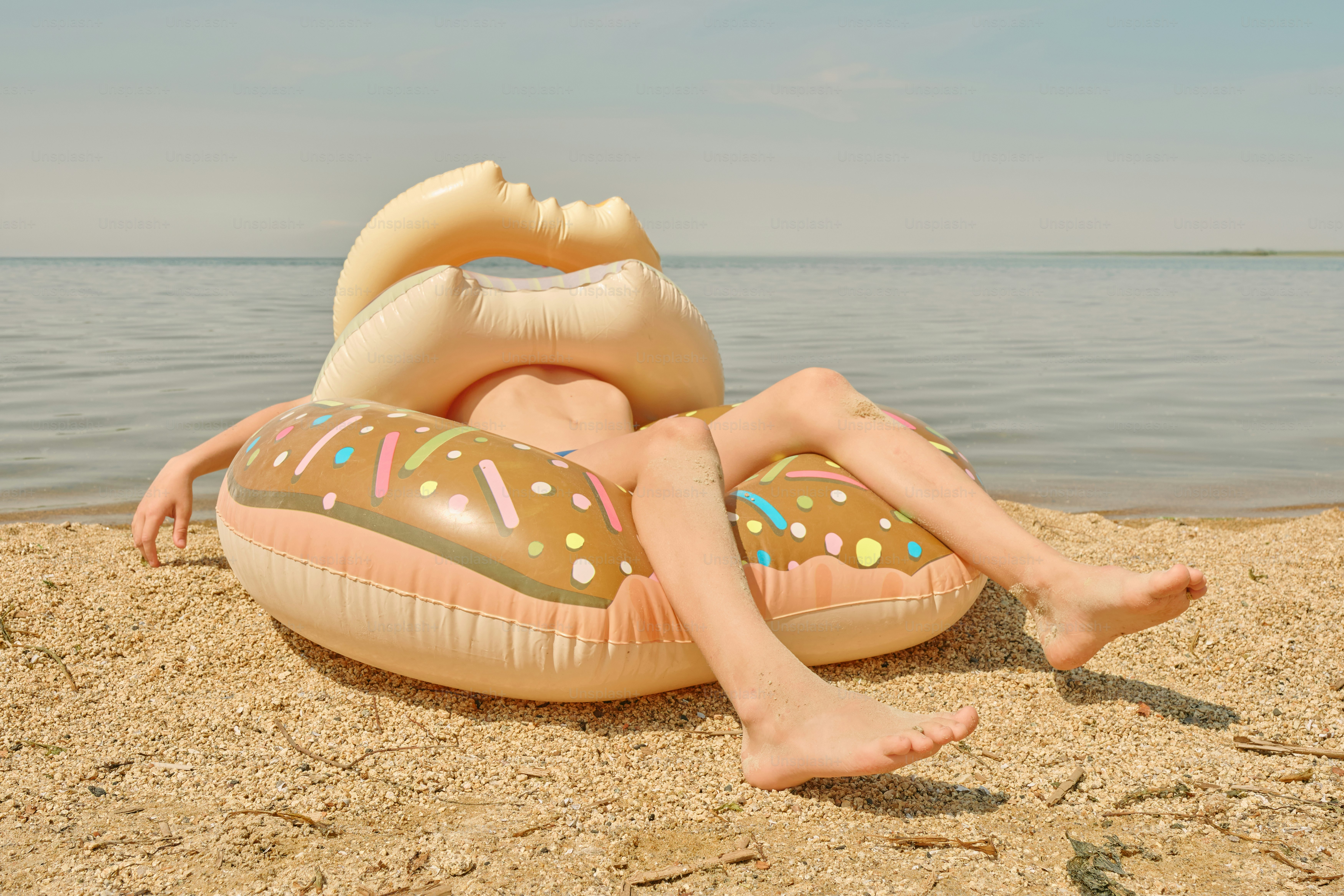 Person relaxes inside an inflatable donut at the beach.