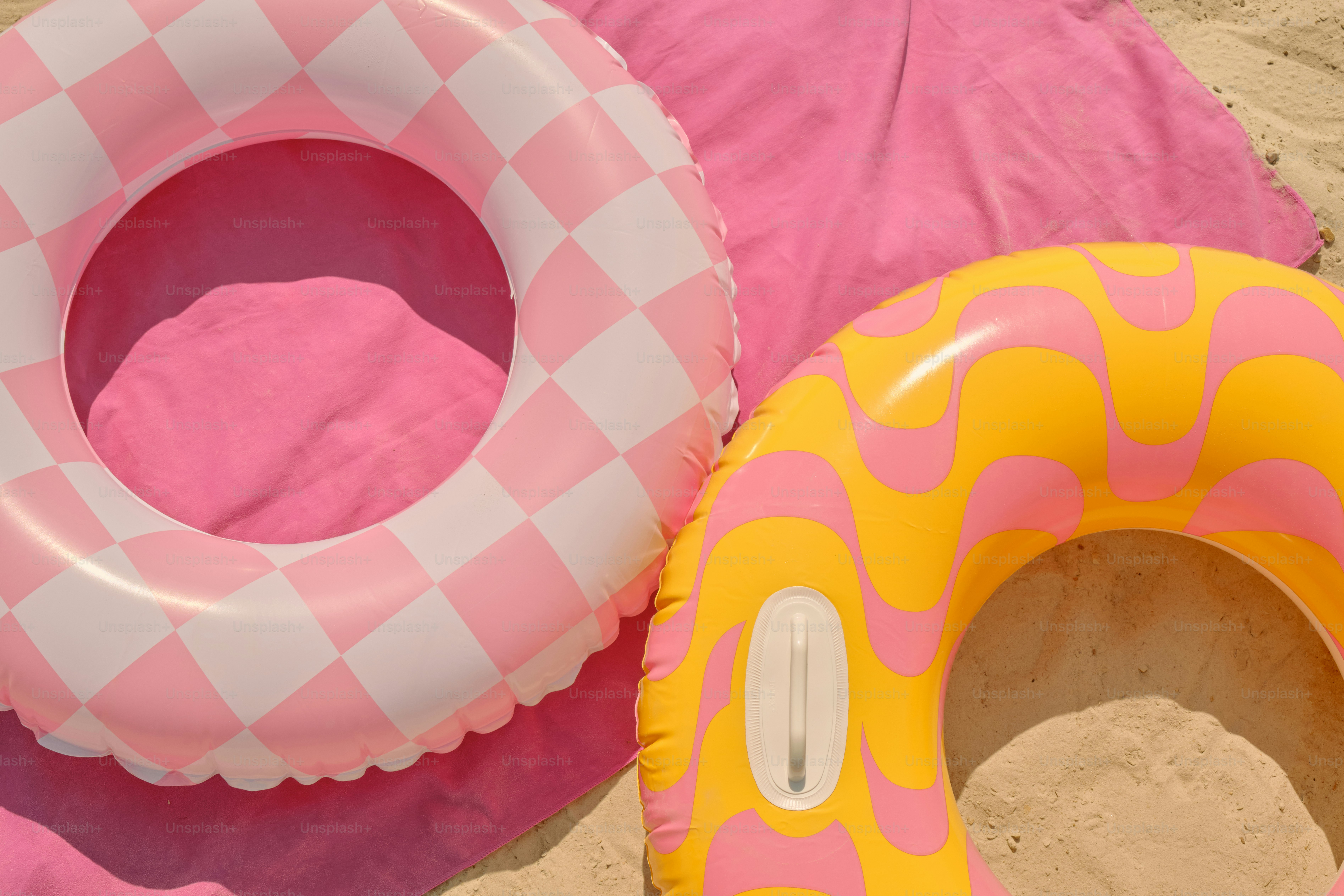 Pink pool floats and towel on sand.