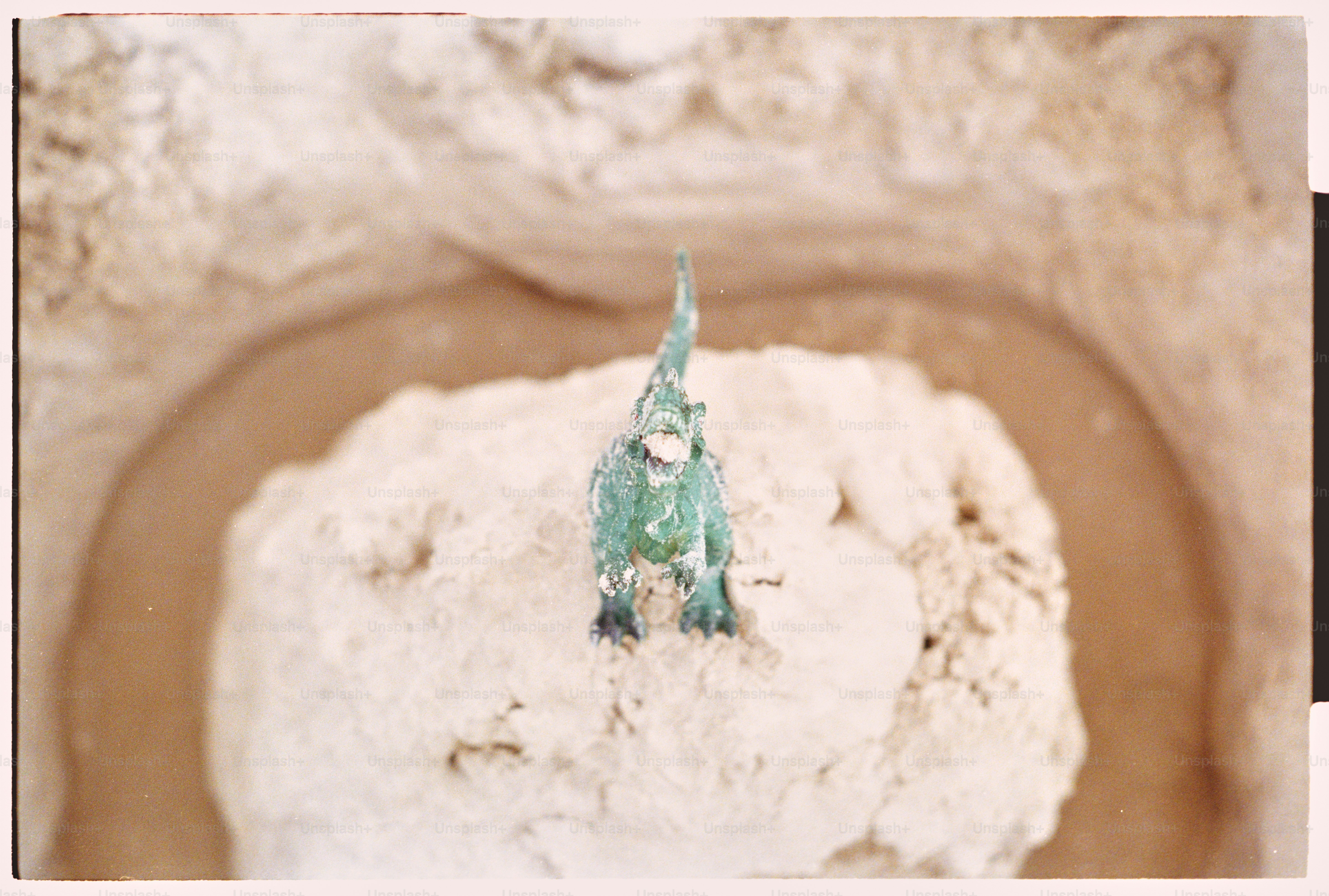 Un dinosaurio verde de juguete se encuentra en un montículo de arena.