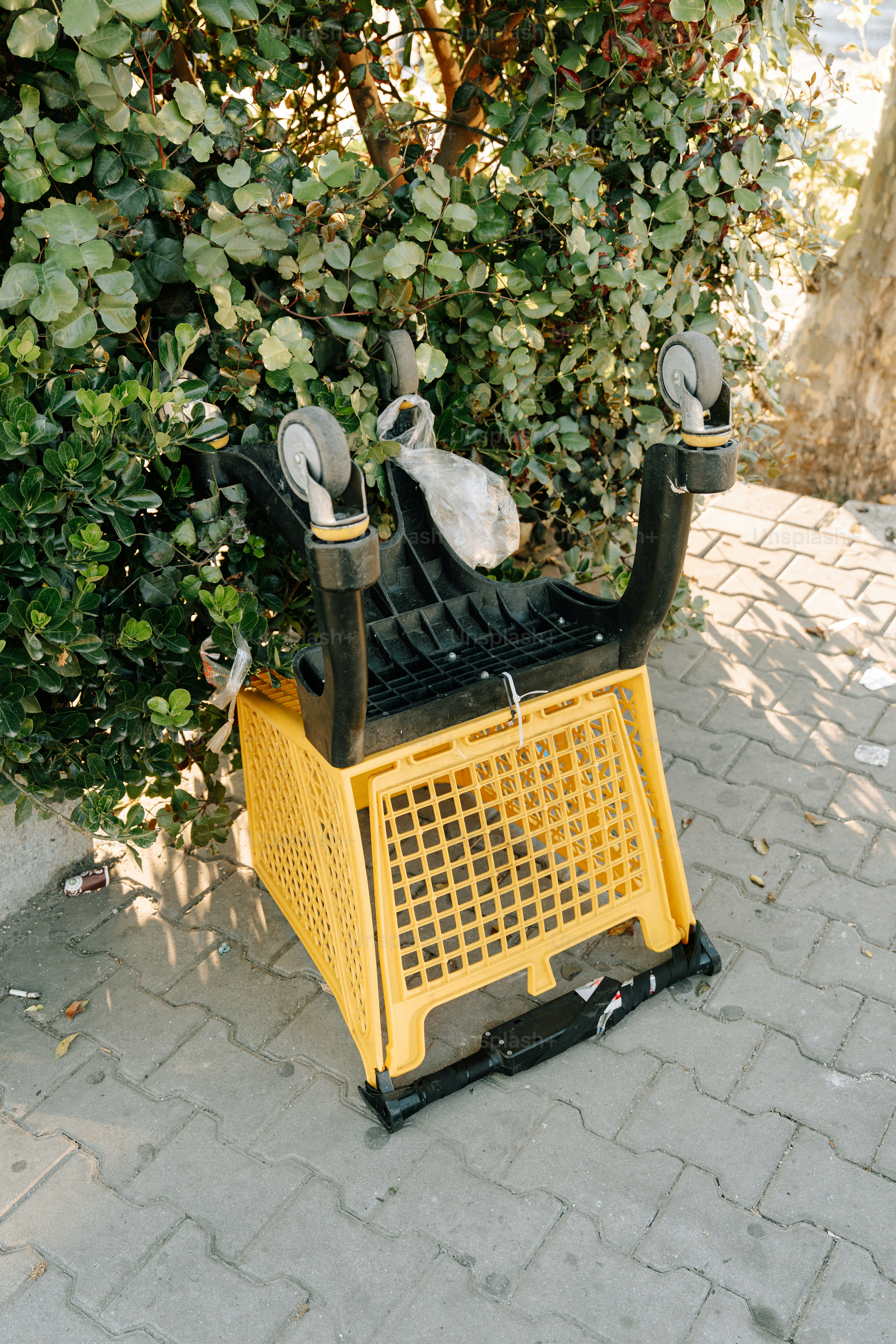 A shopping cart is upside down by some bushes.