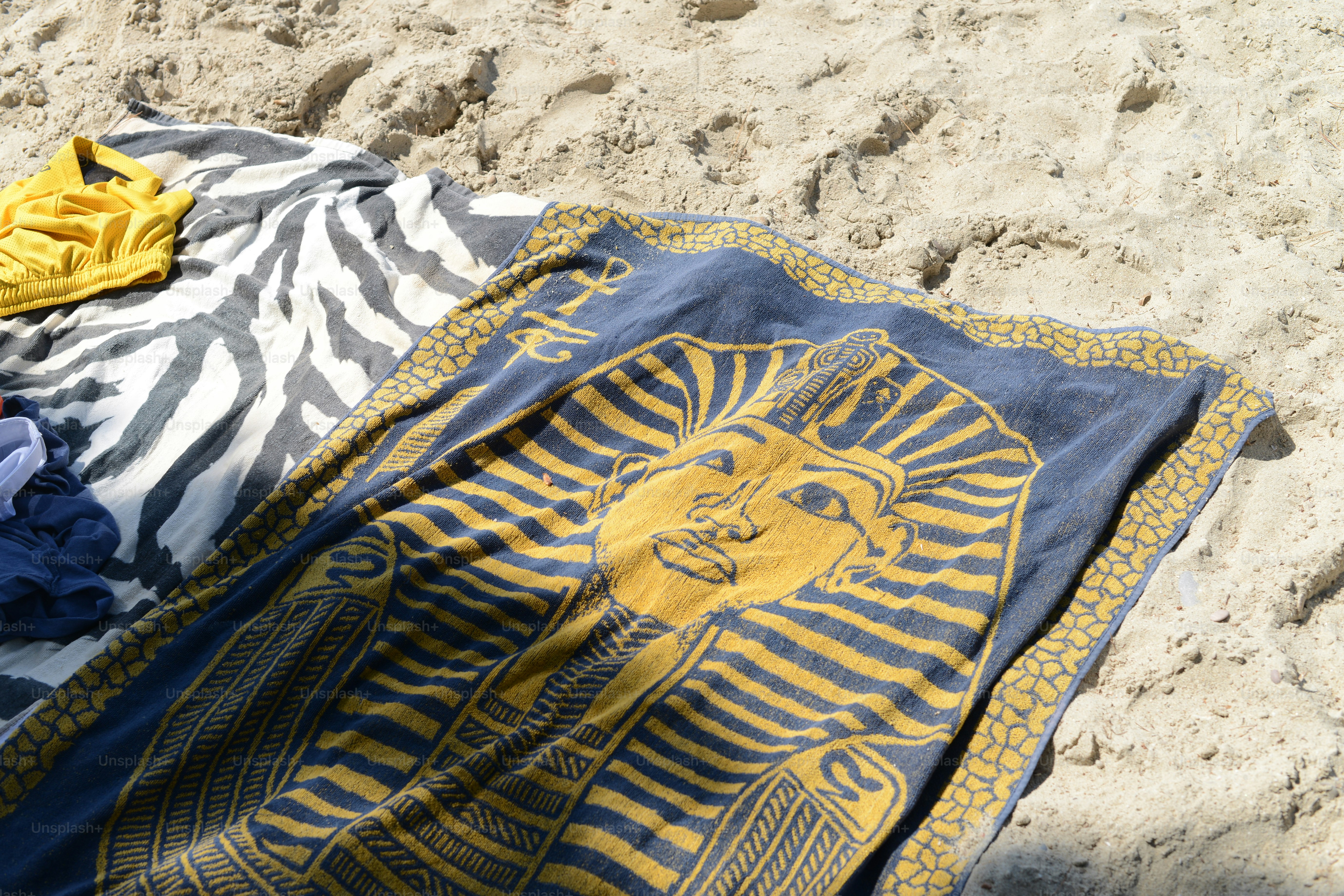 Beach towels with designs lie on the sand.