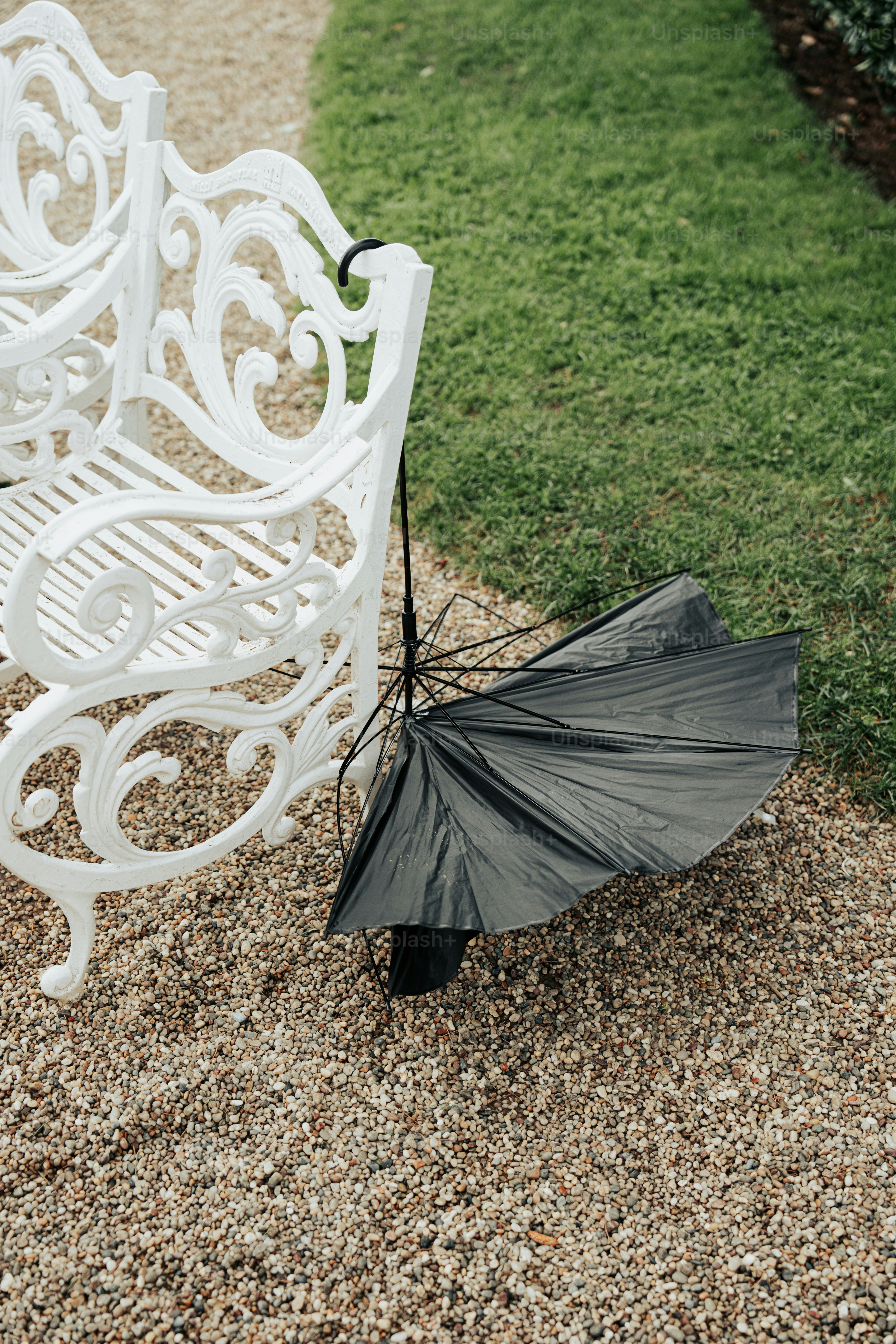 Un paraguas negro descansa junto a un banco blanco.