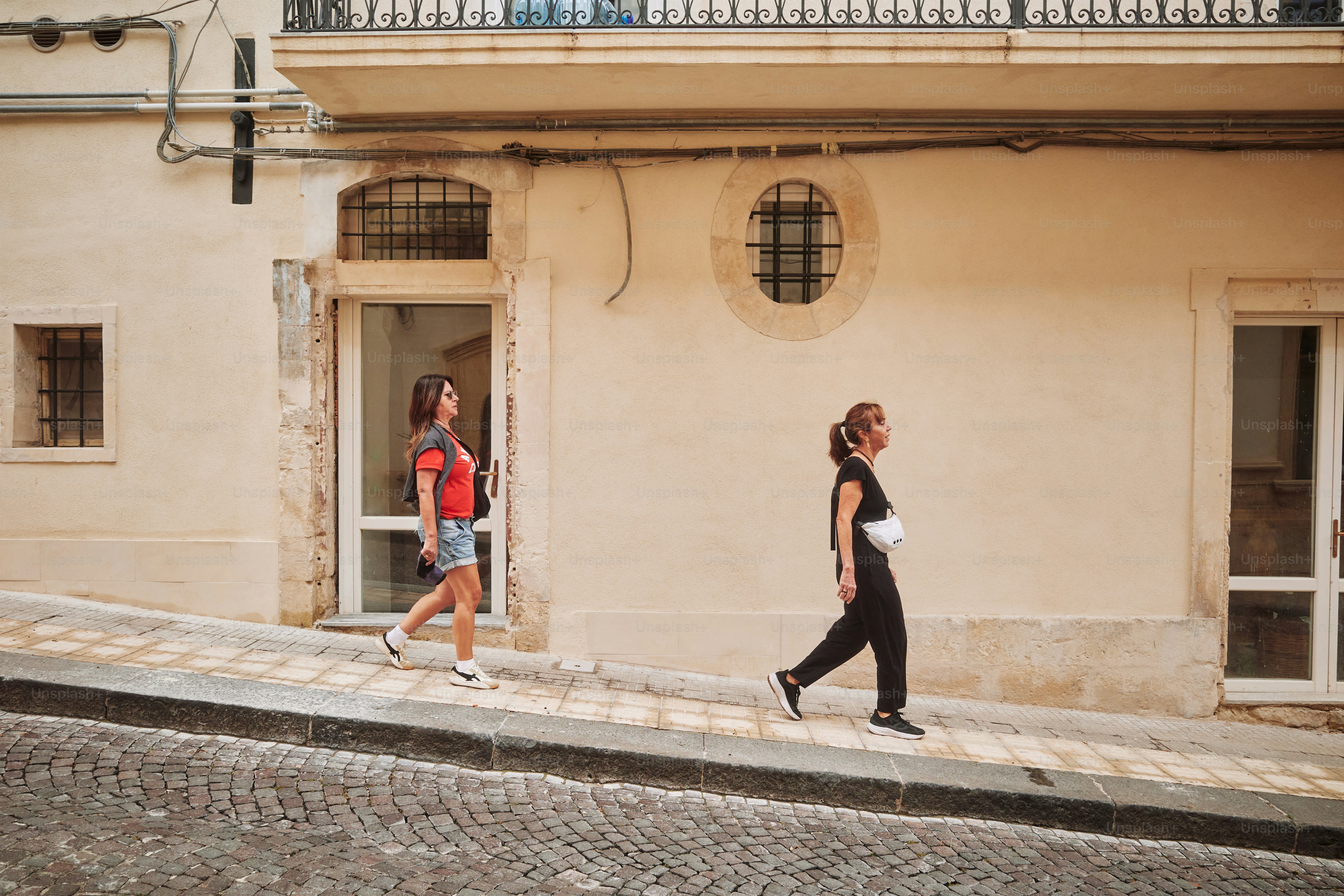 Dos mujeres caminan por una calle soleada e inclinada.