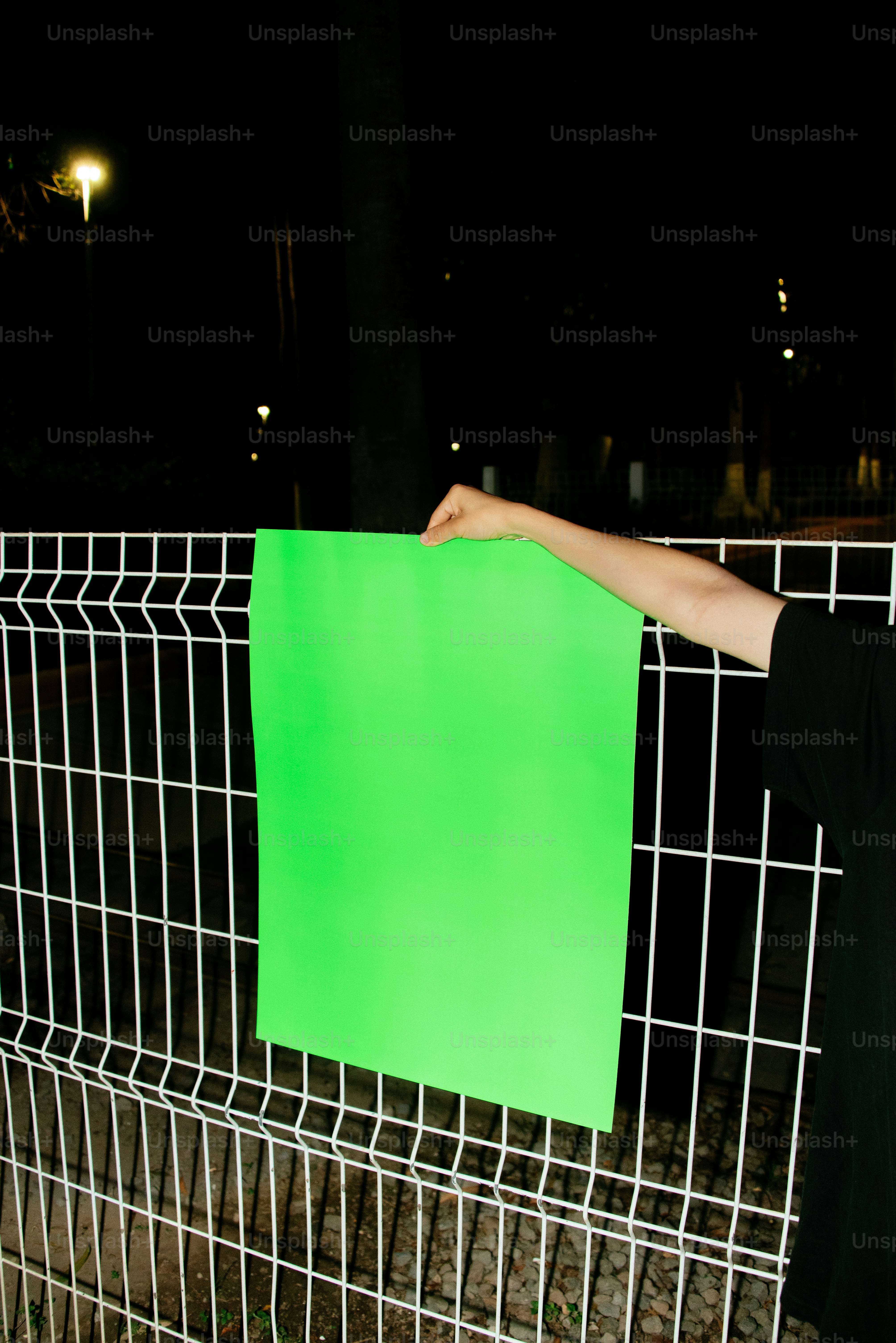 Hand holds a green sign on a fence at night.
