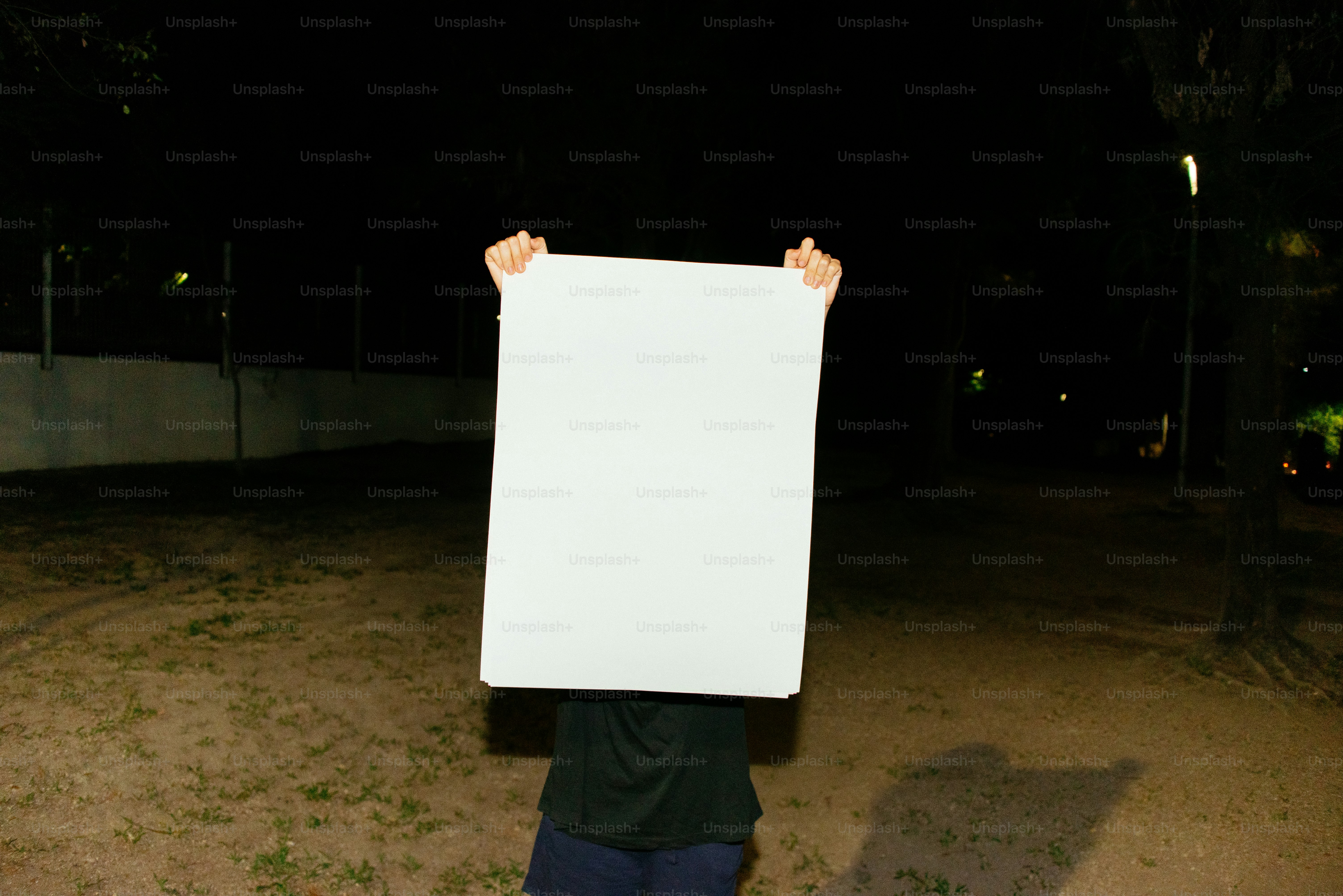 Person holds a blank white sign at night.