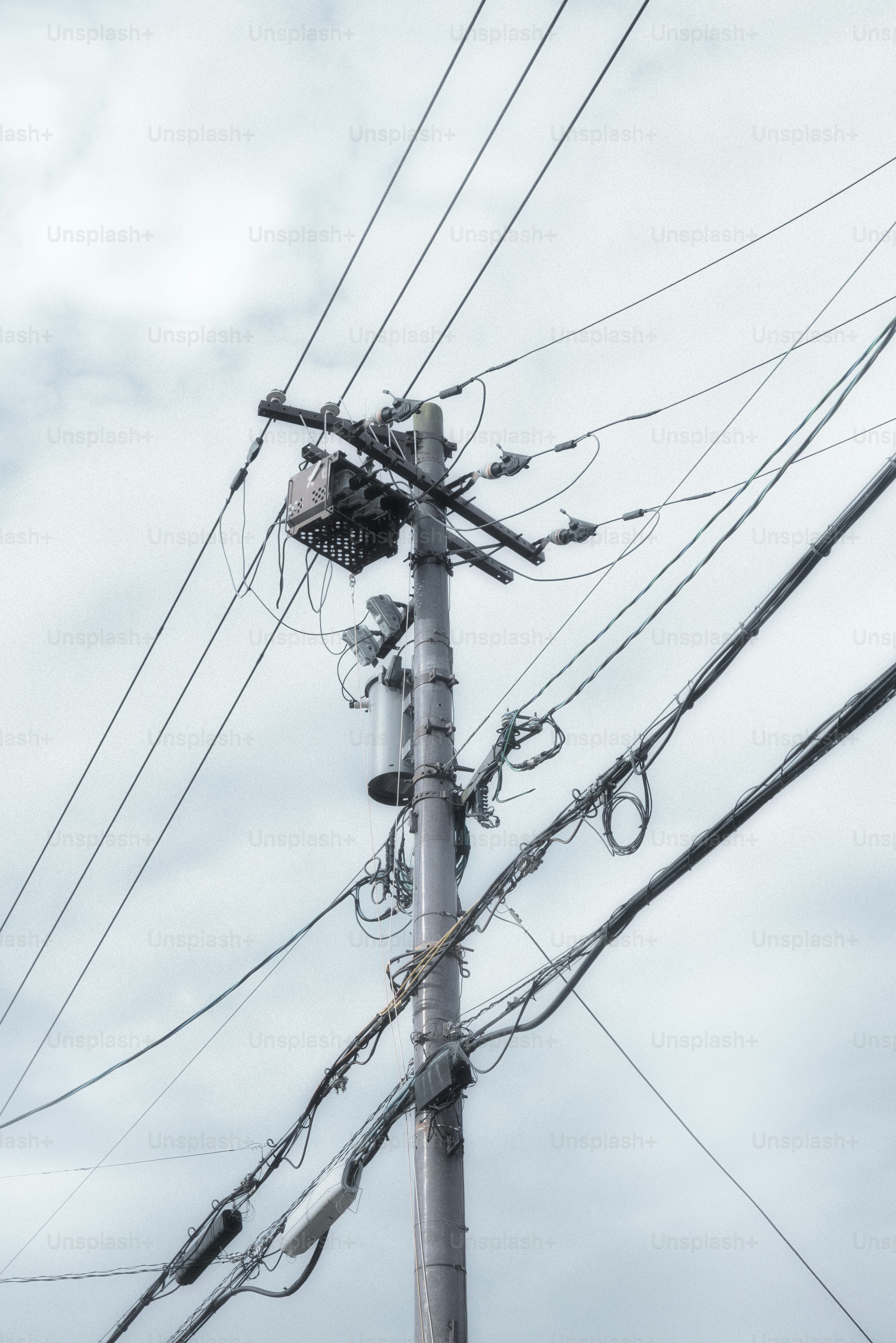 Power lines crisscross a pole against a cloudy sky.