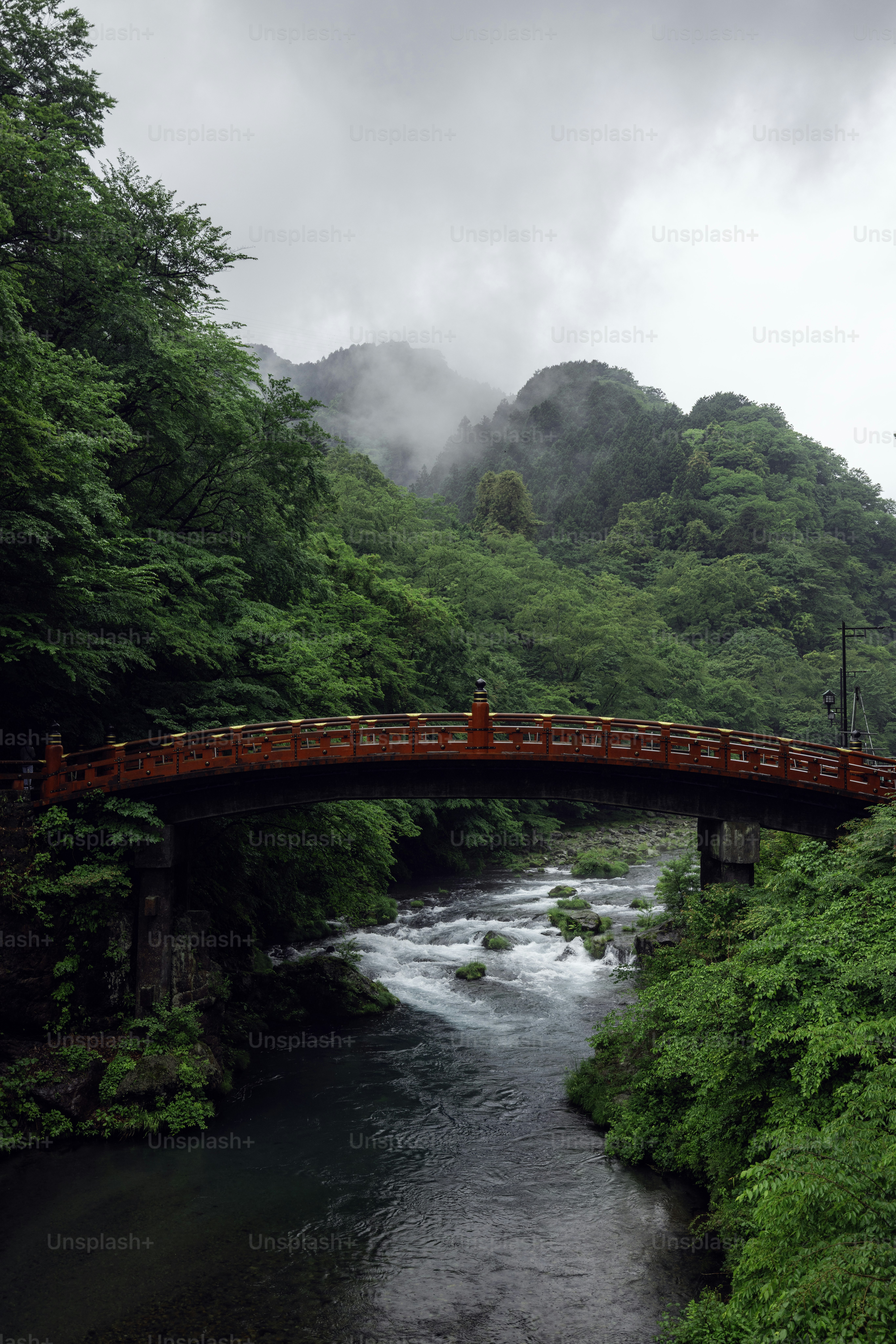 A red bridge arches over a rushing river.