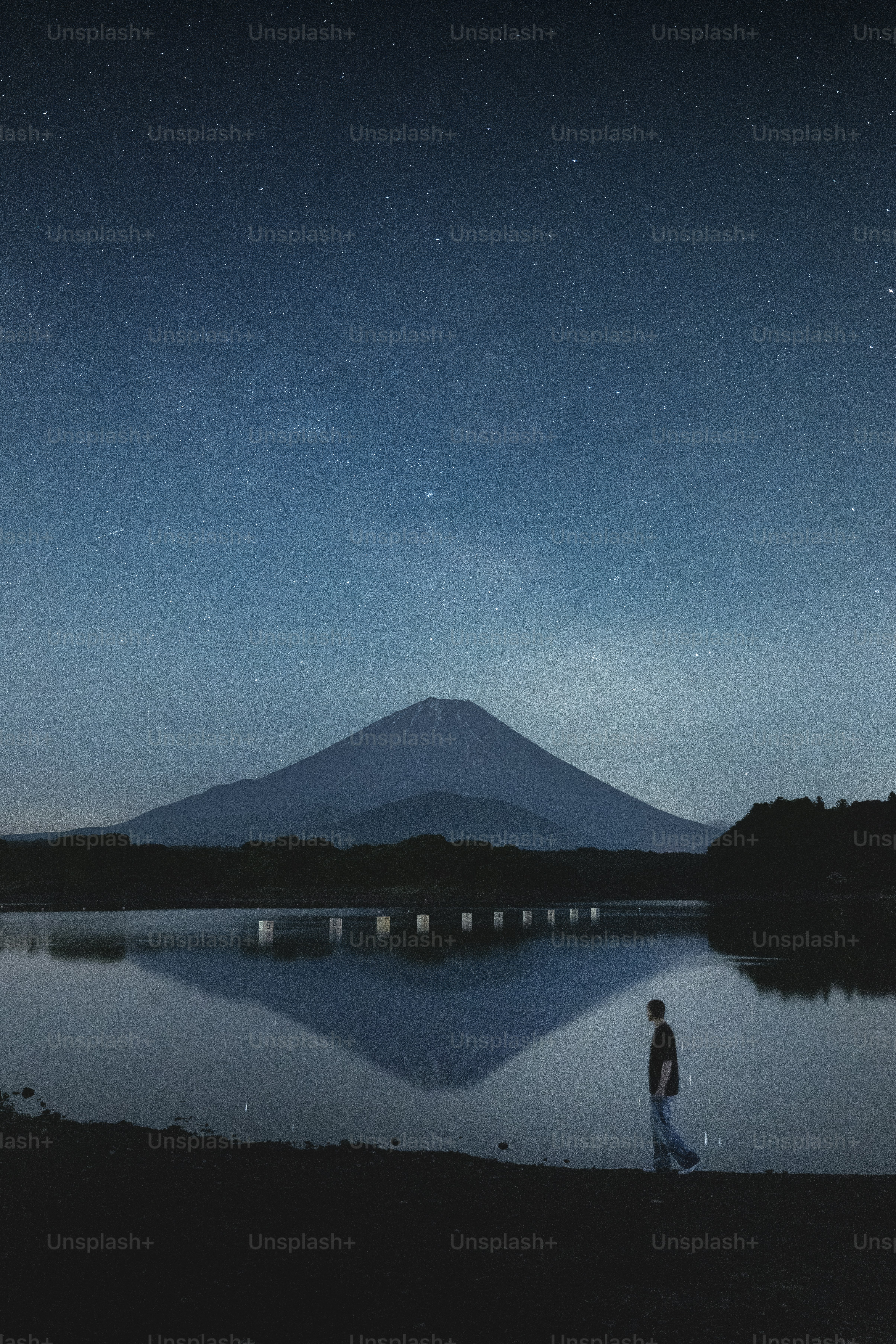 A person walks before a mountain under stars.