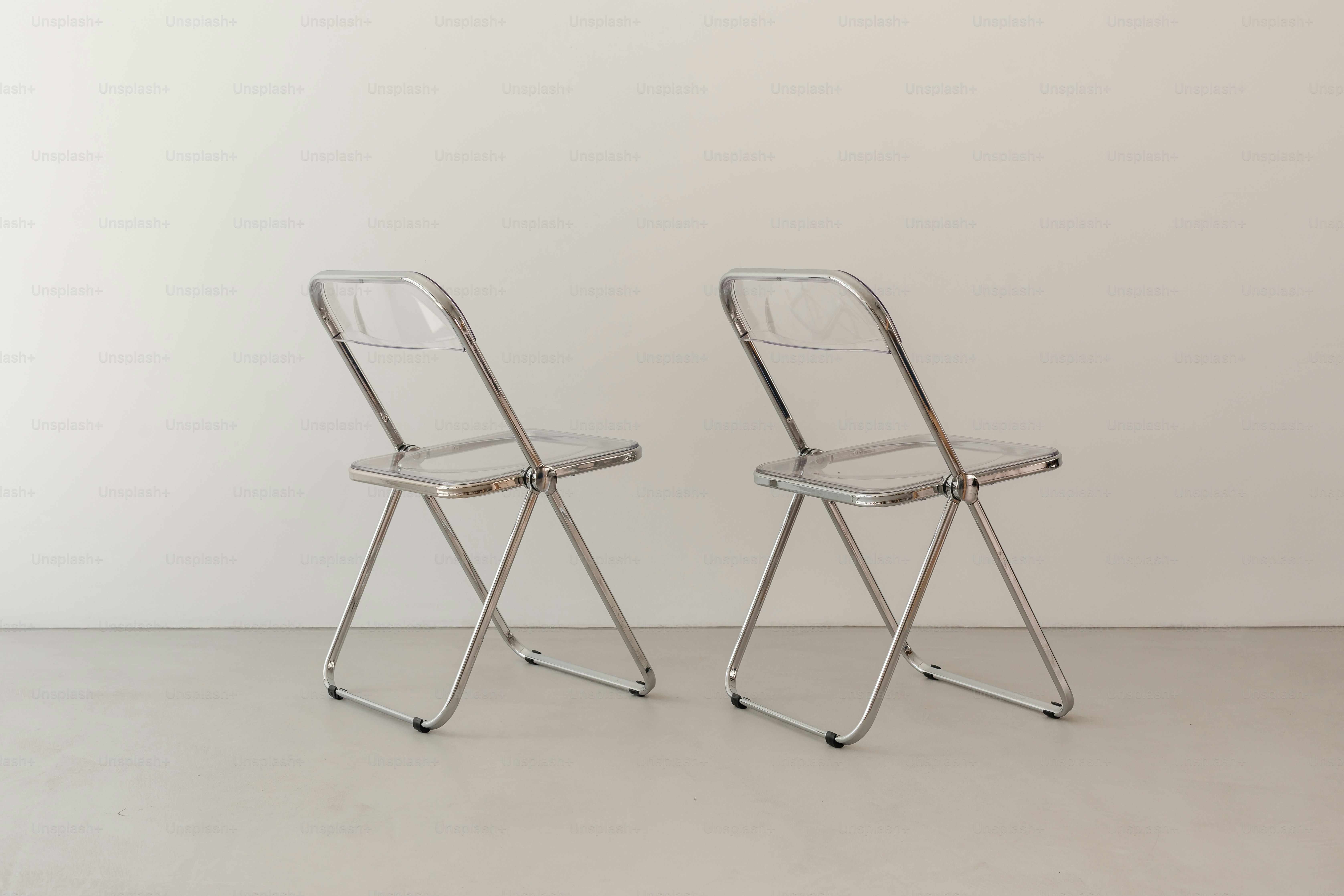 Zwei durchsichtige Klappstühle stehen vor einer weißen Wand.