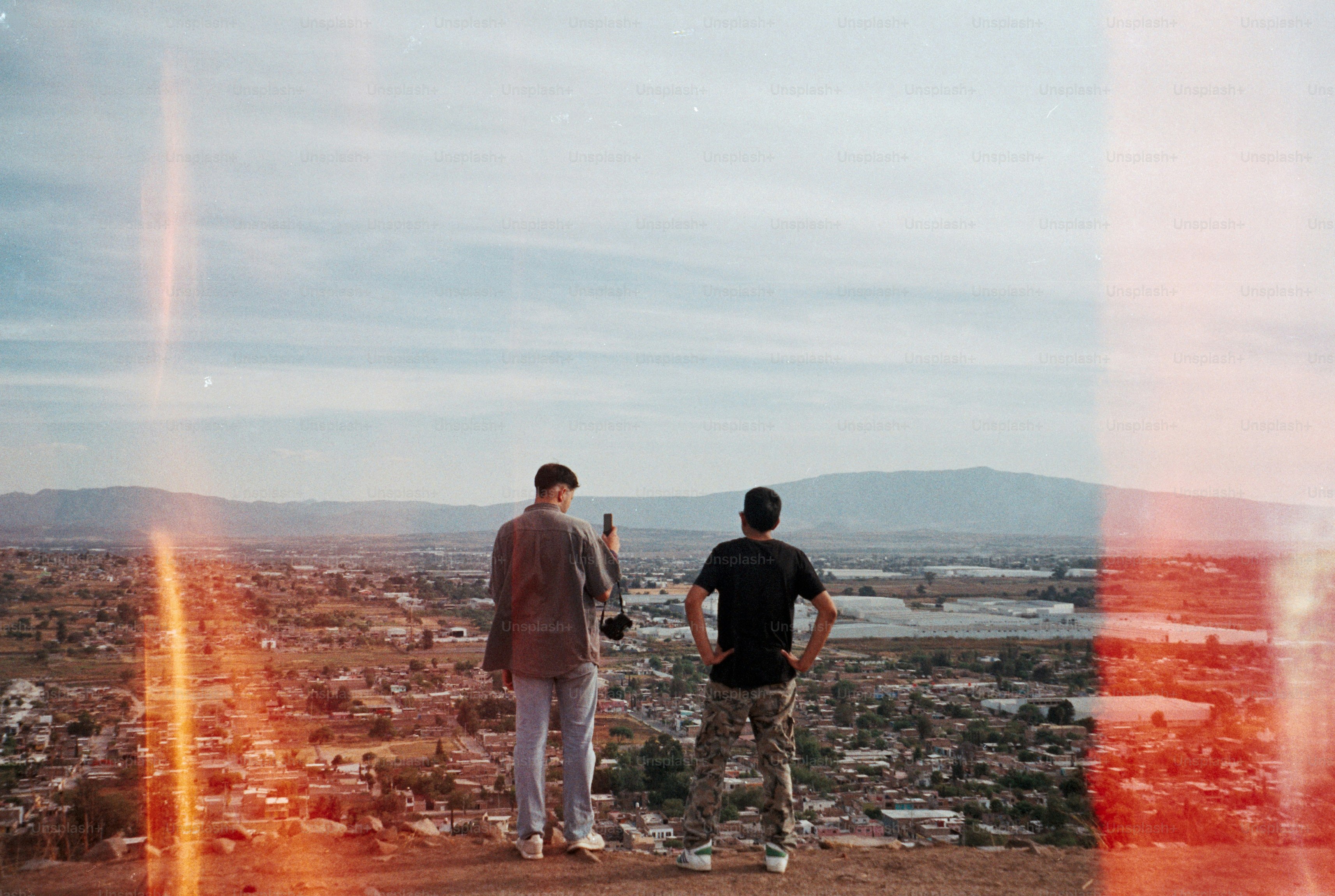 Two brothers standing apart on a quiet rooftop at sunset, city skyline behind them, neither able to look the other in the eyes.