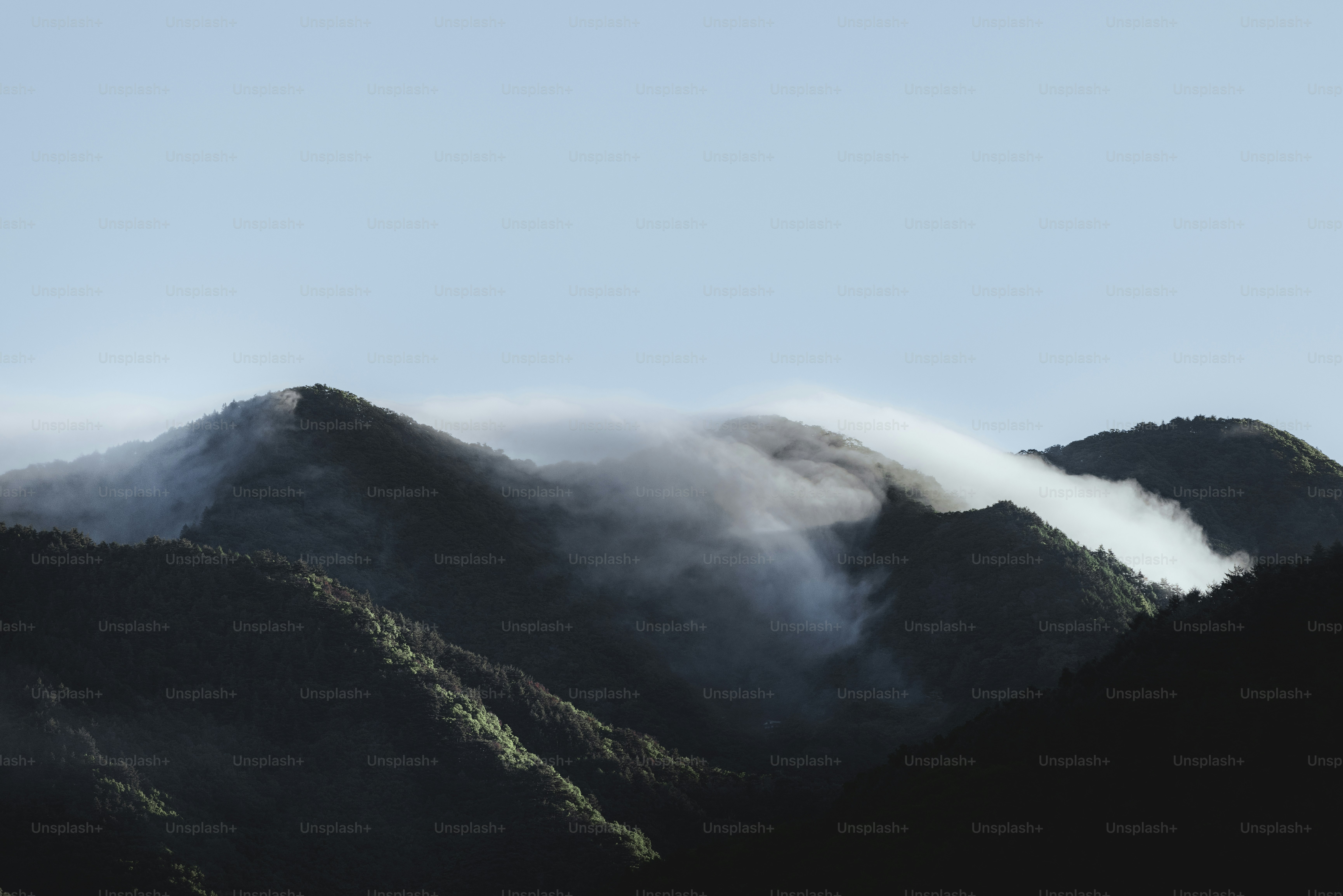 Mountains peak with mist, under a blue sky.