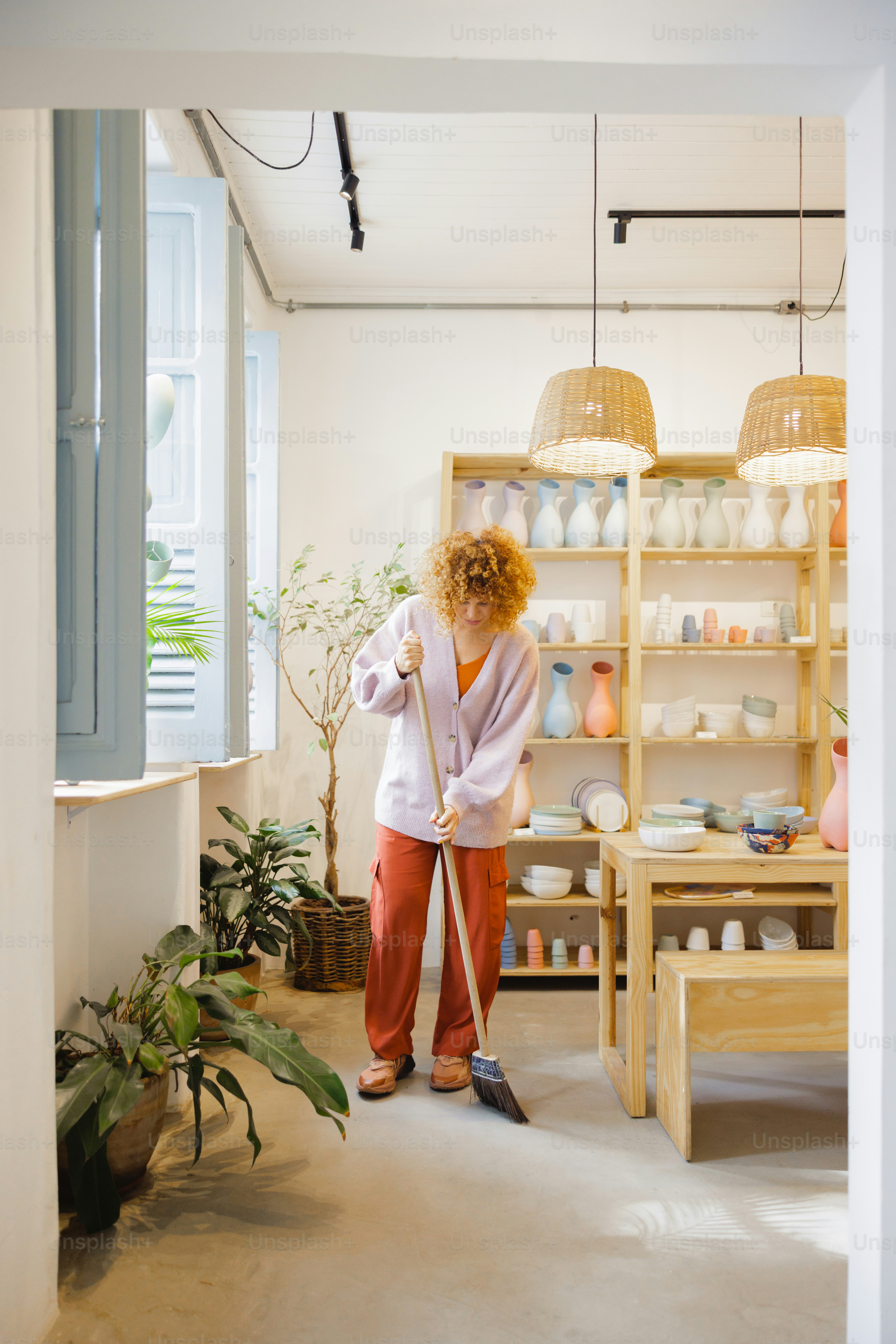 Woman sweeps a floor in a brightly lit shop.