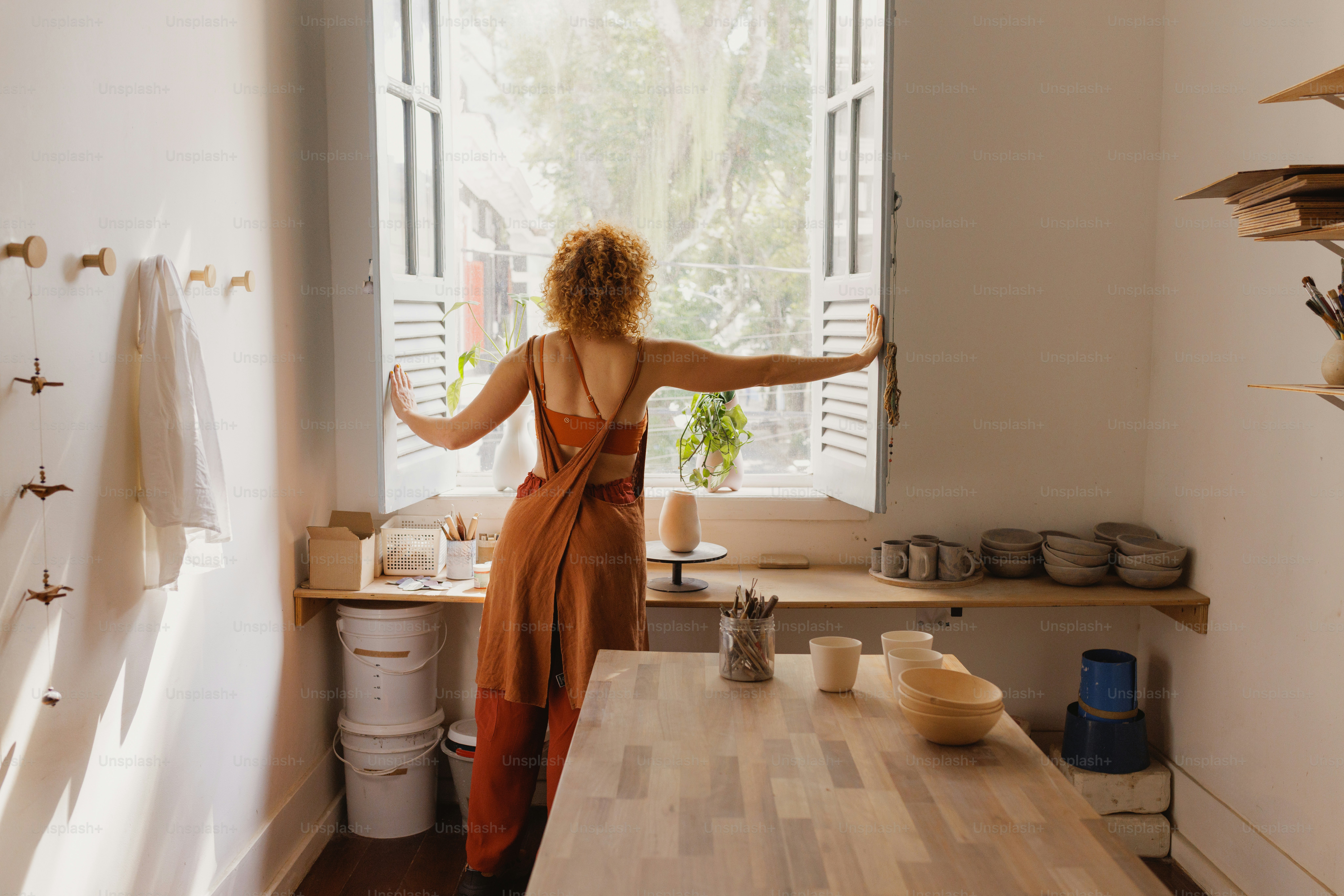 Woman opens a window in her pottery studio.