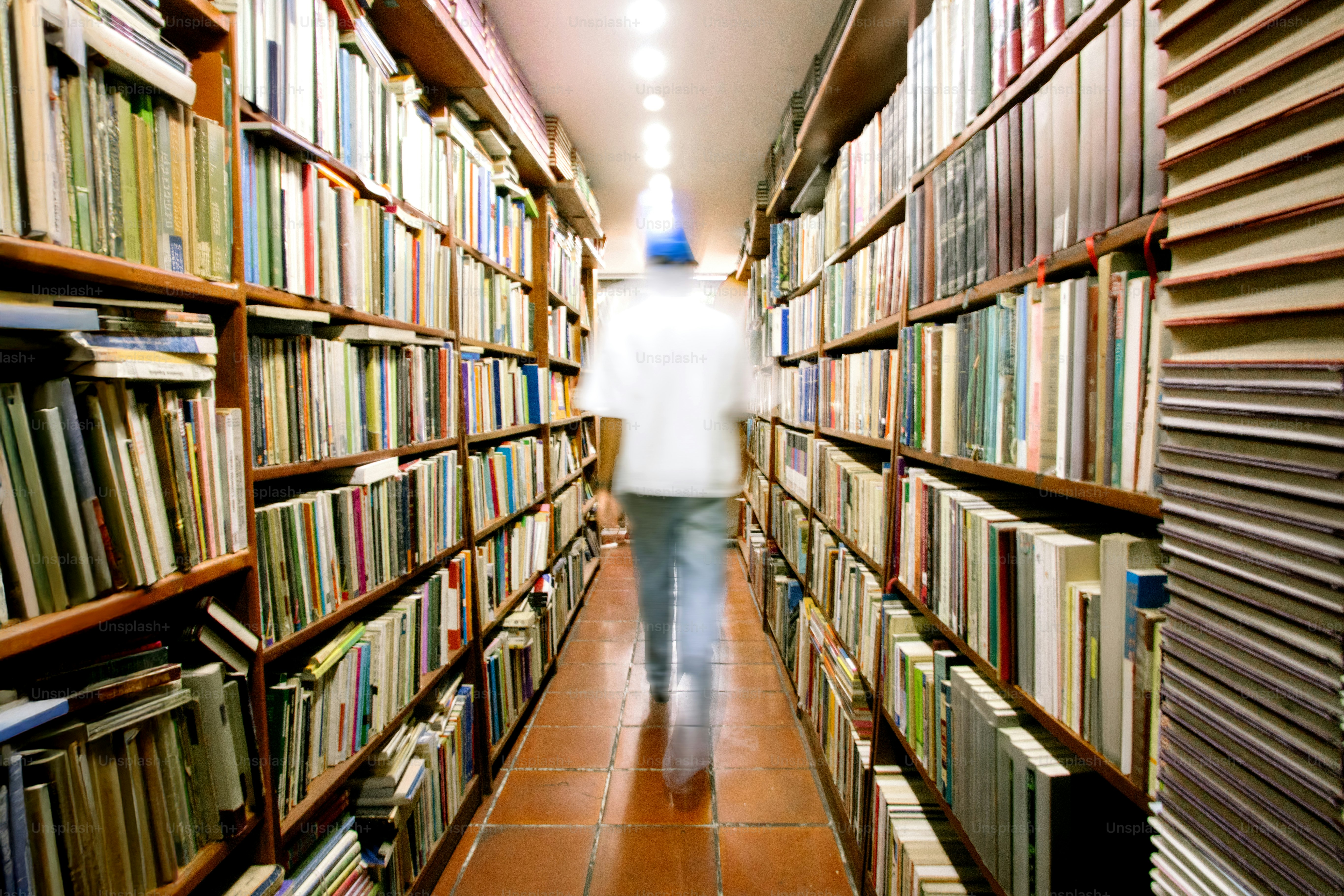 La persona camina por el pasillo de libros de una biblioteca.