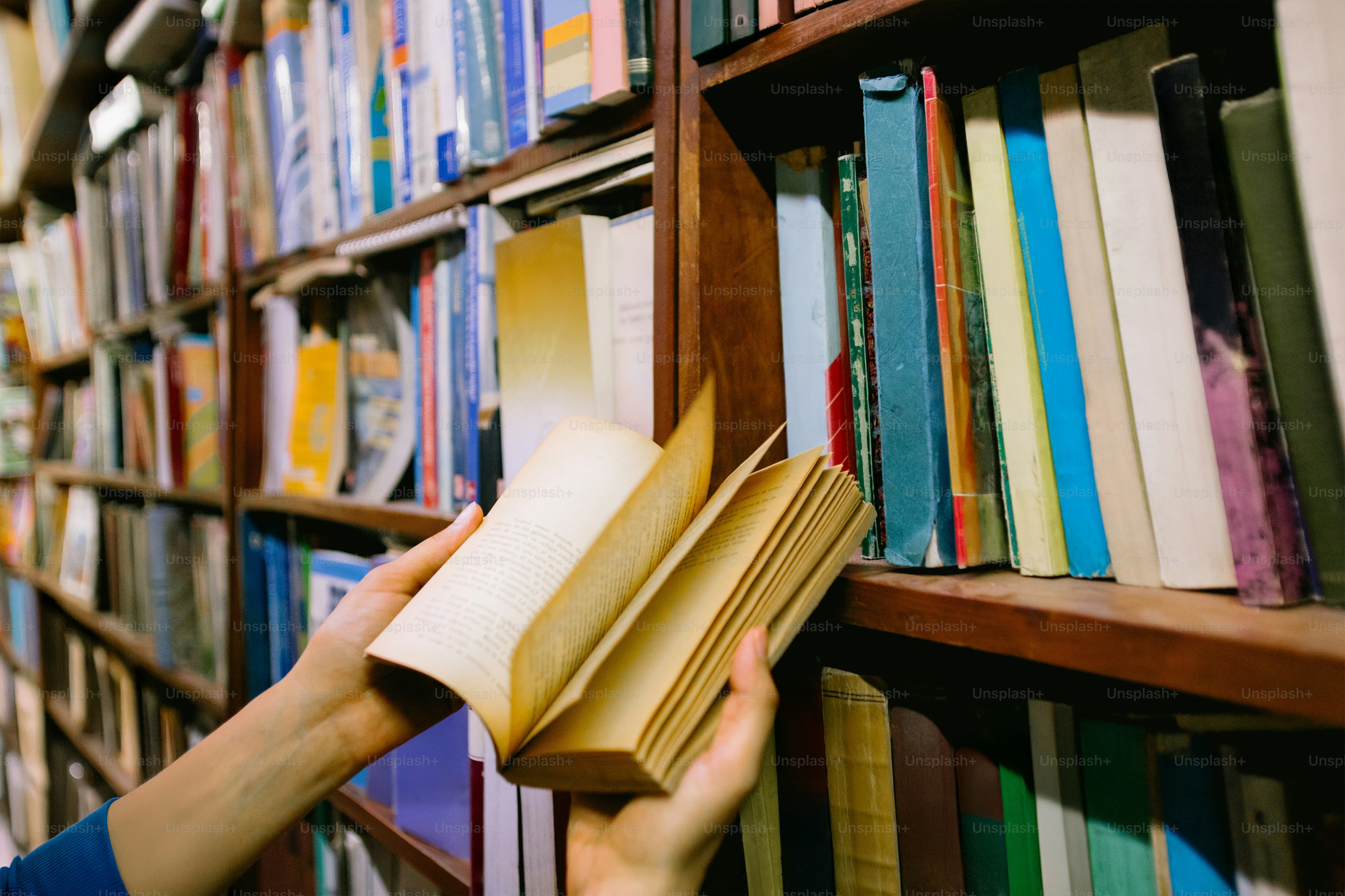 Alguien sostiene un libro abierto cerca de una estantería.