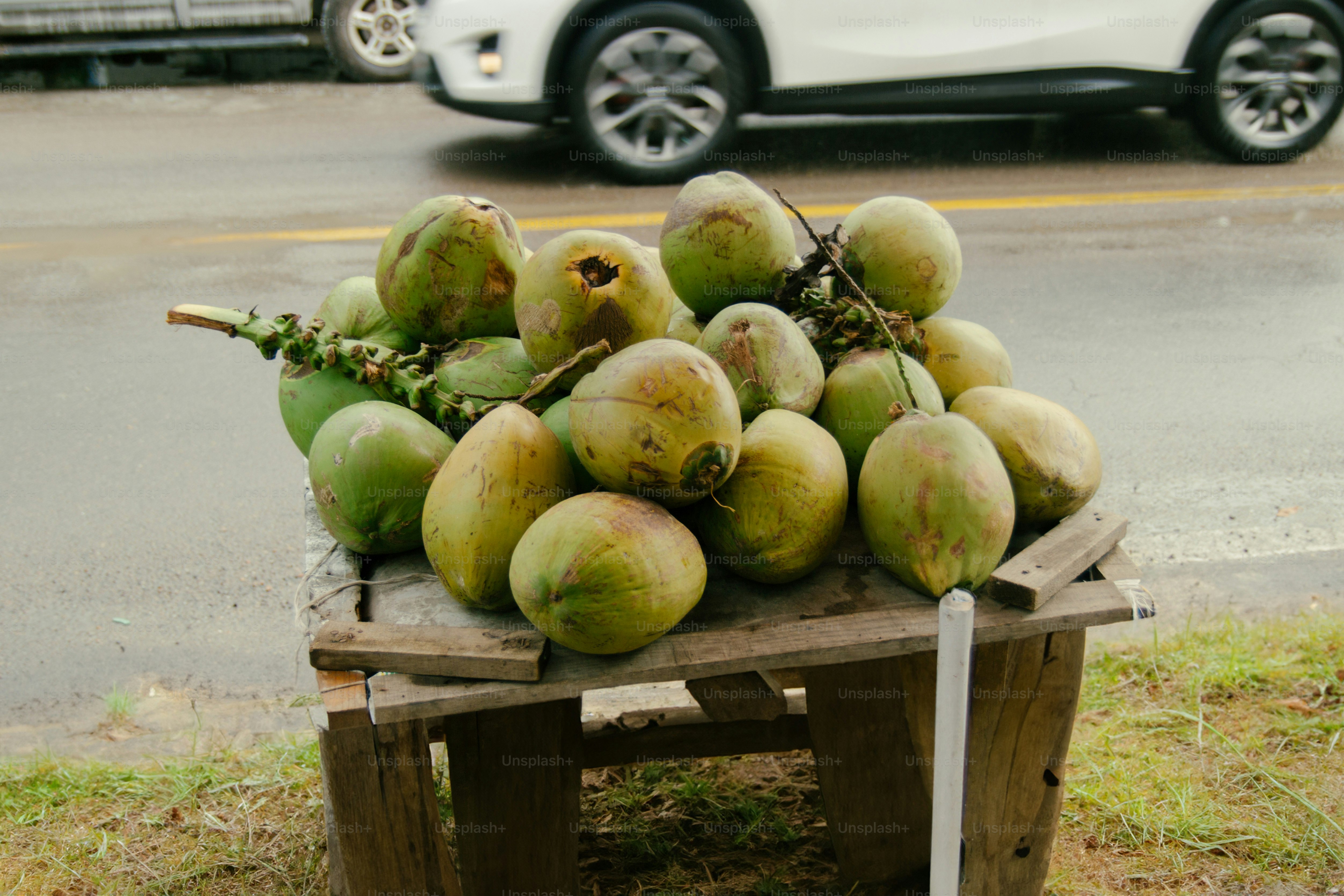 Coconuts are piled on a wooden table outside.