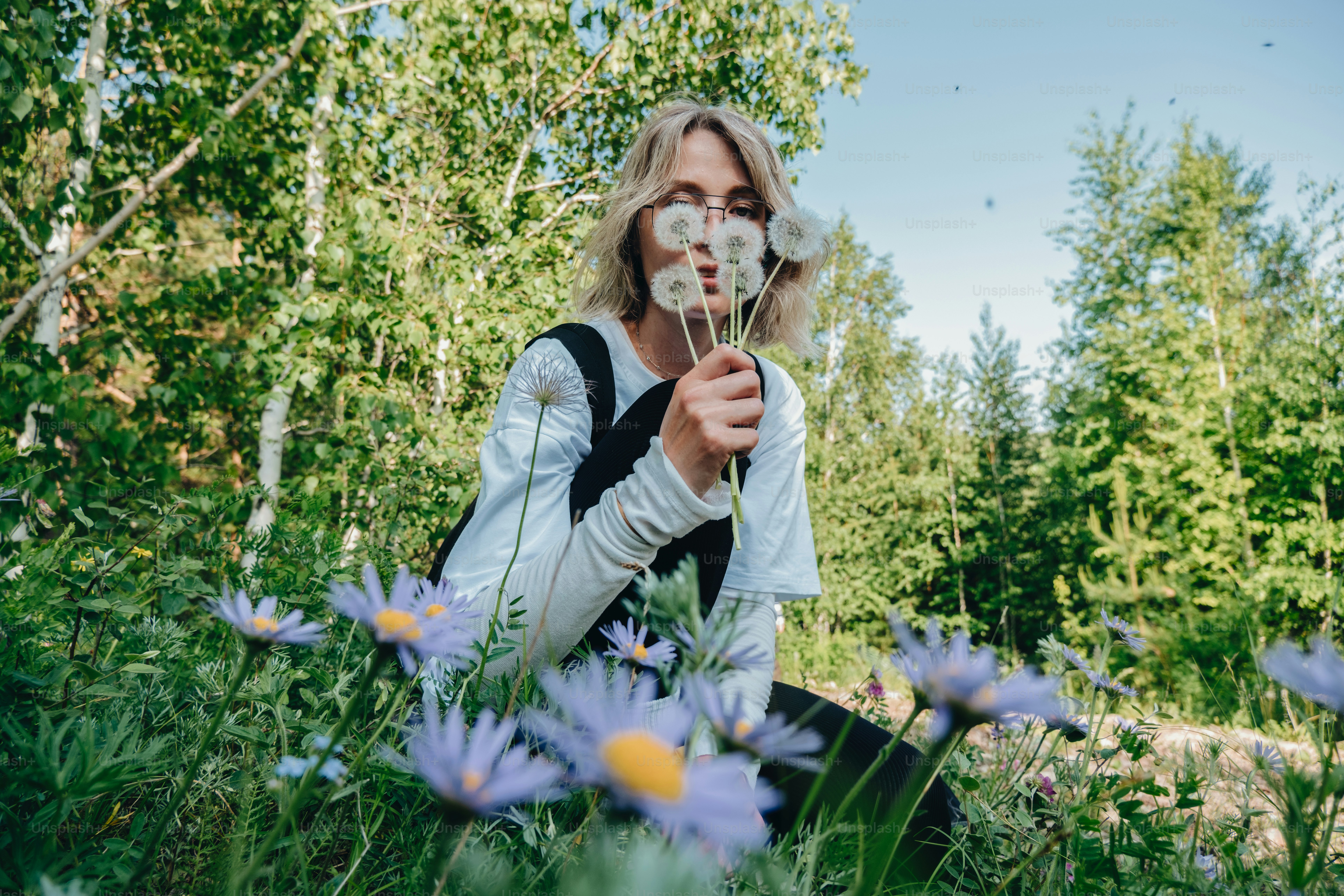Woman playfully hides behind dandelions in a field.