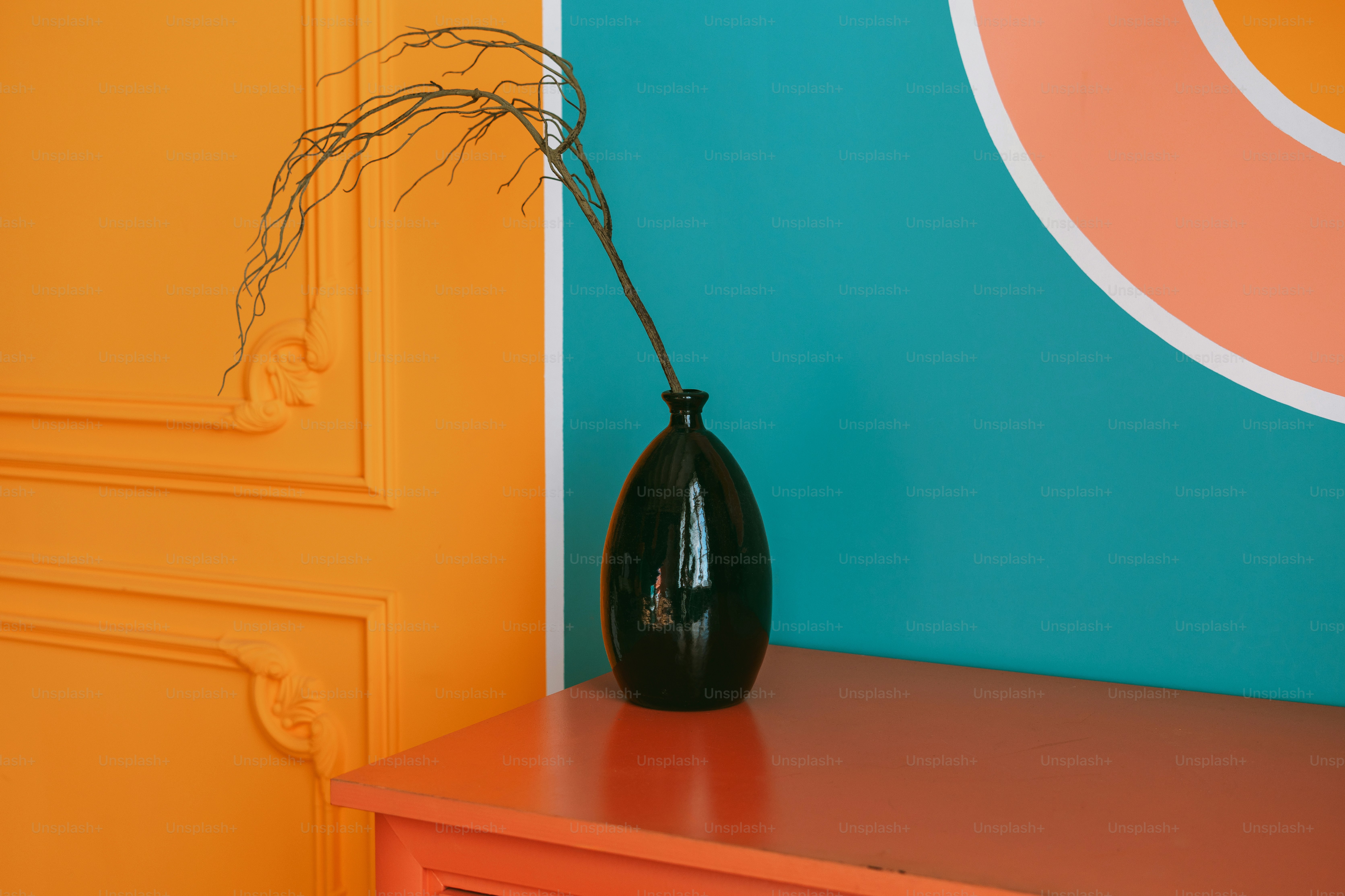 A black vase holds a branch against colorful walls.