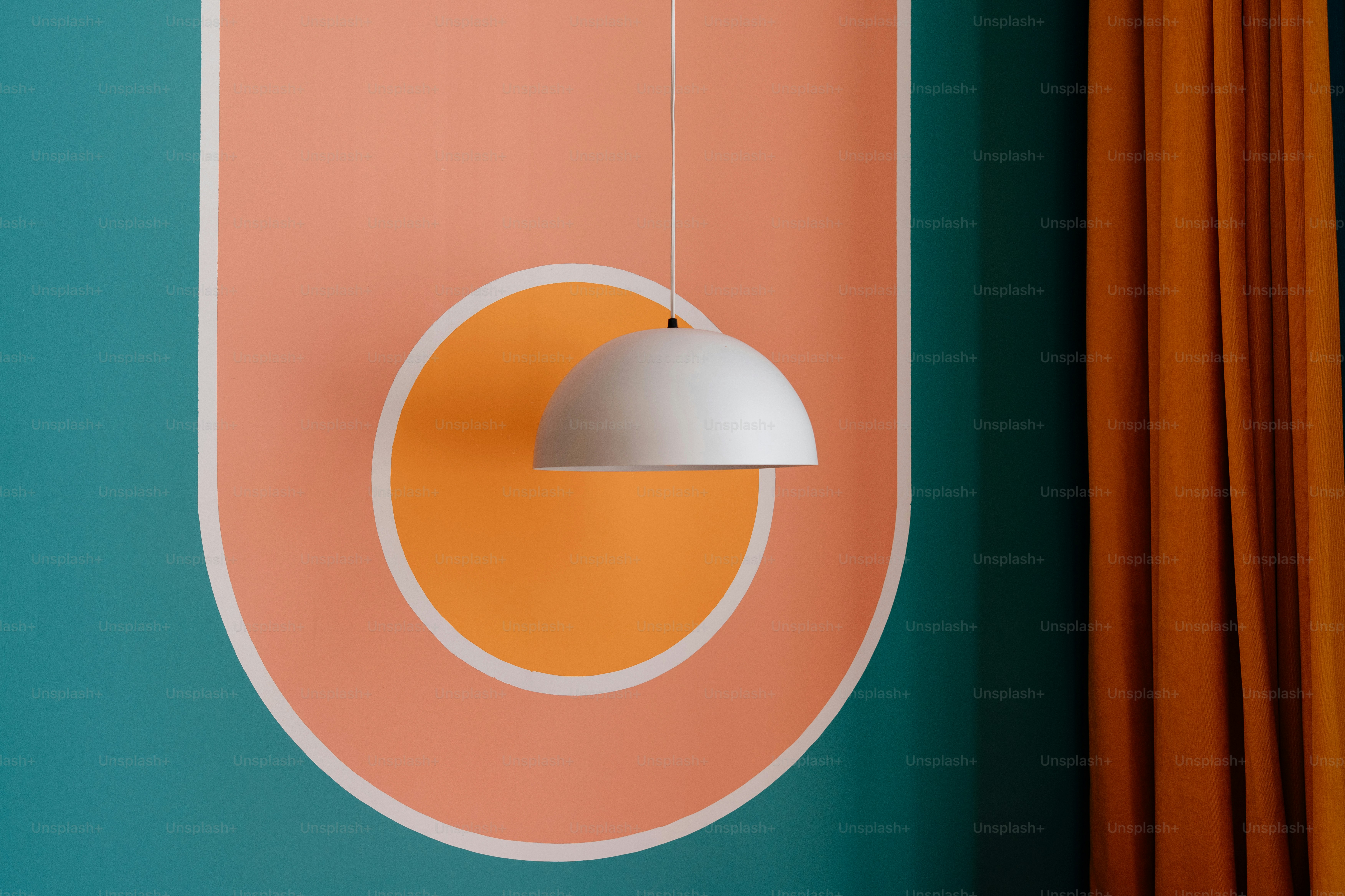 A modern lamp hangs in front of a colorful wall.