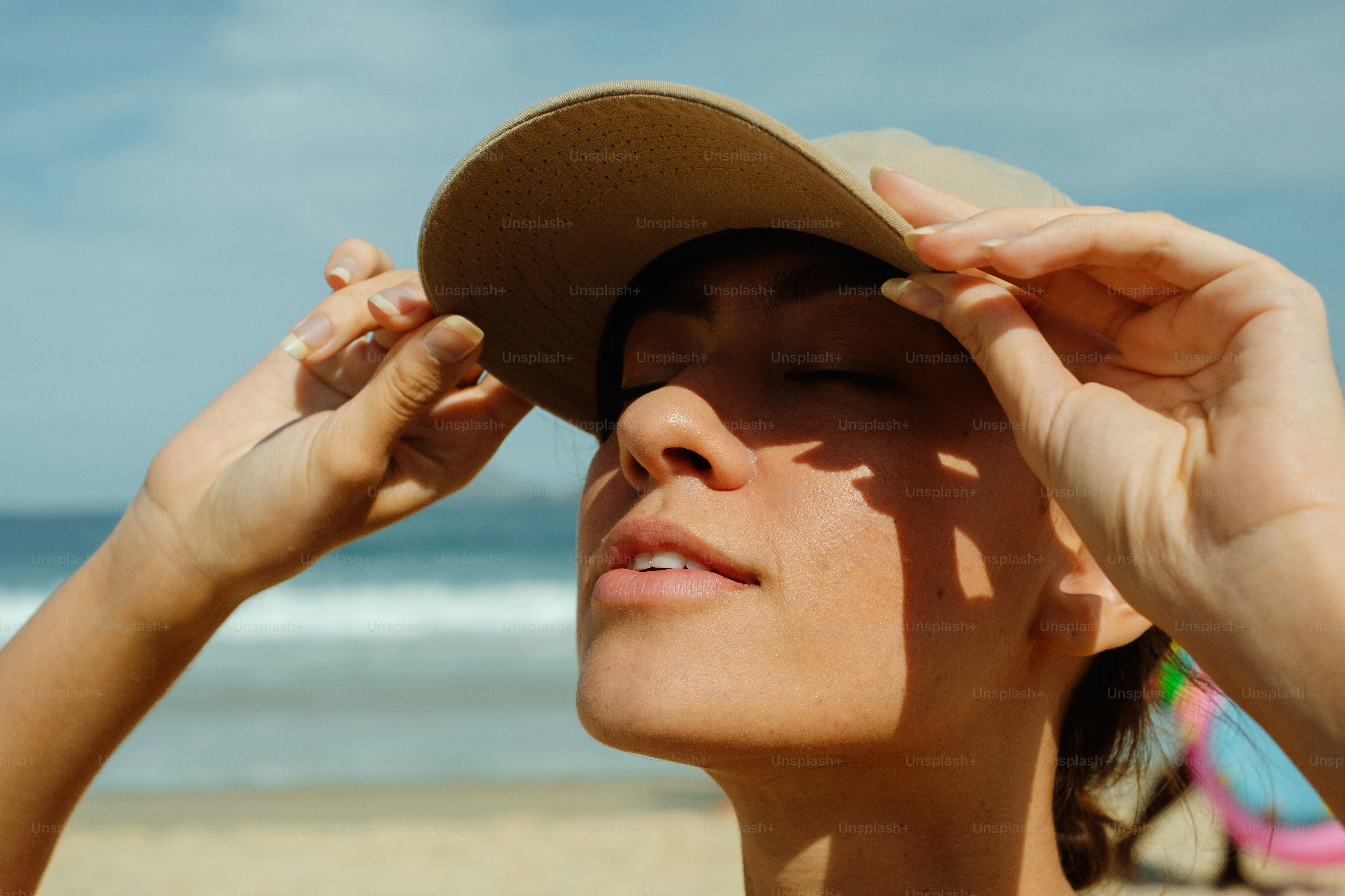 La femme ajuste son chapeau à la plage, profitant du soleil.