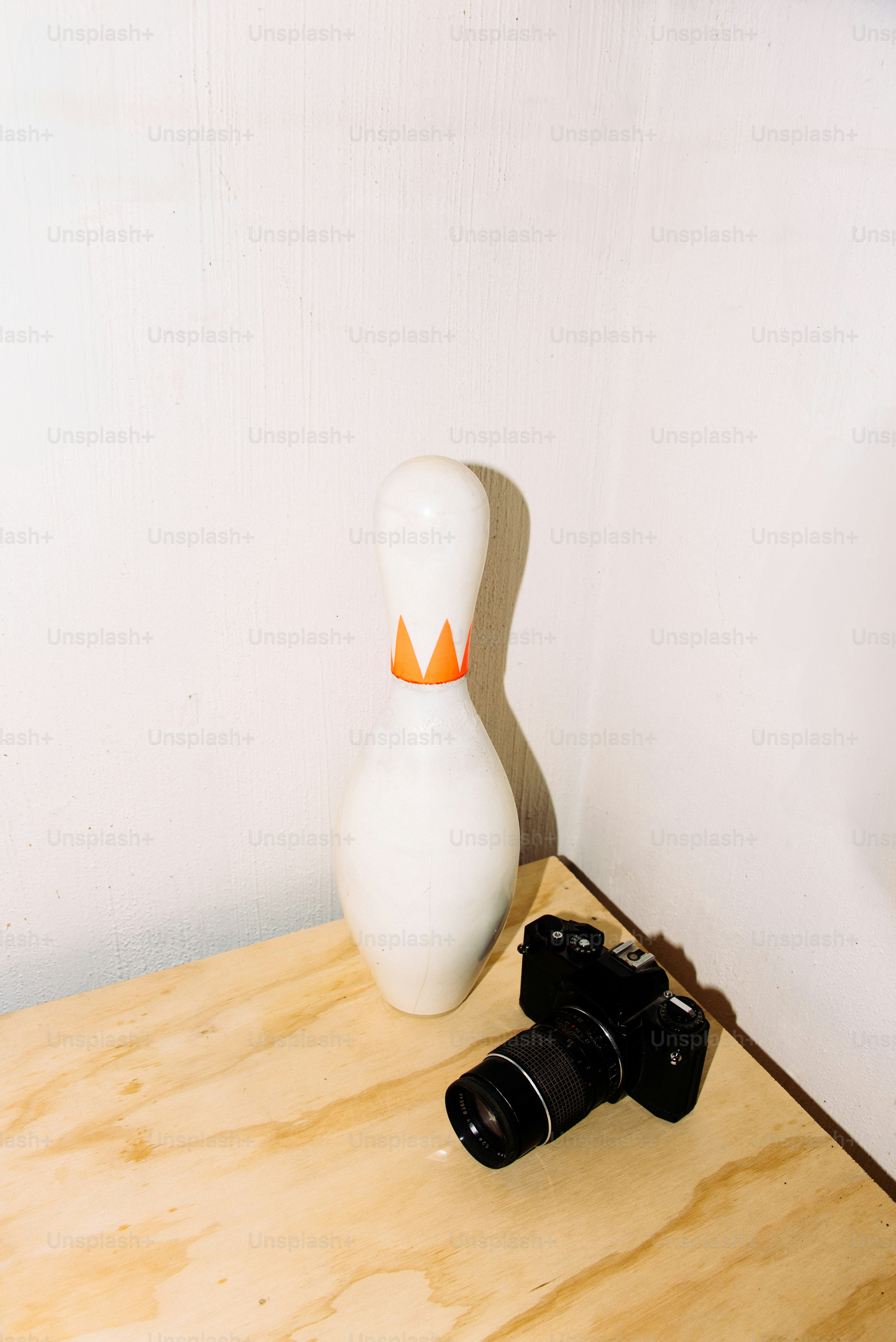 A bowling pin and camera stand next to each other.