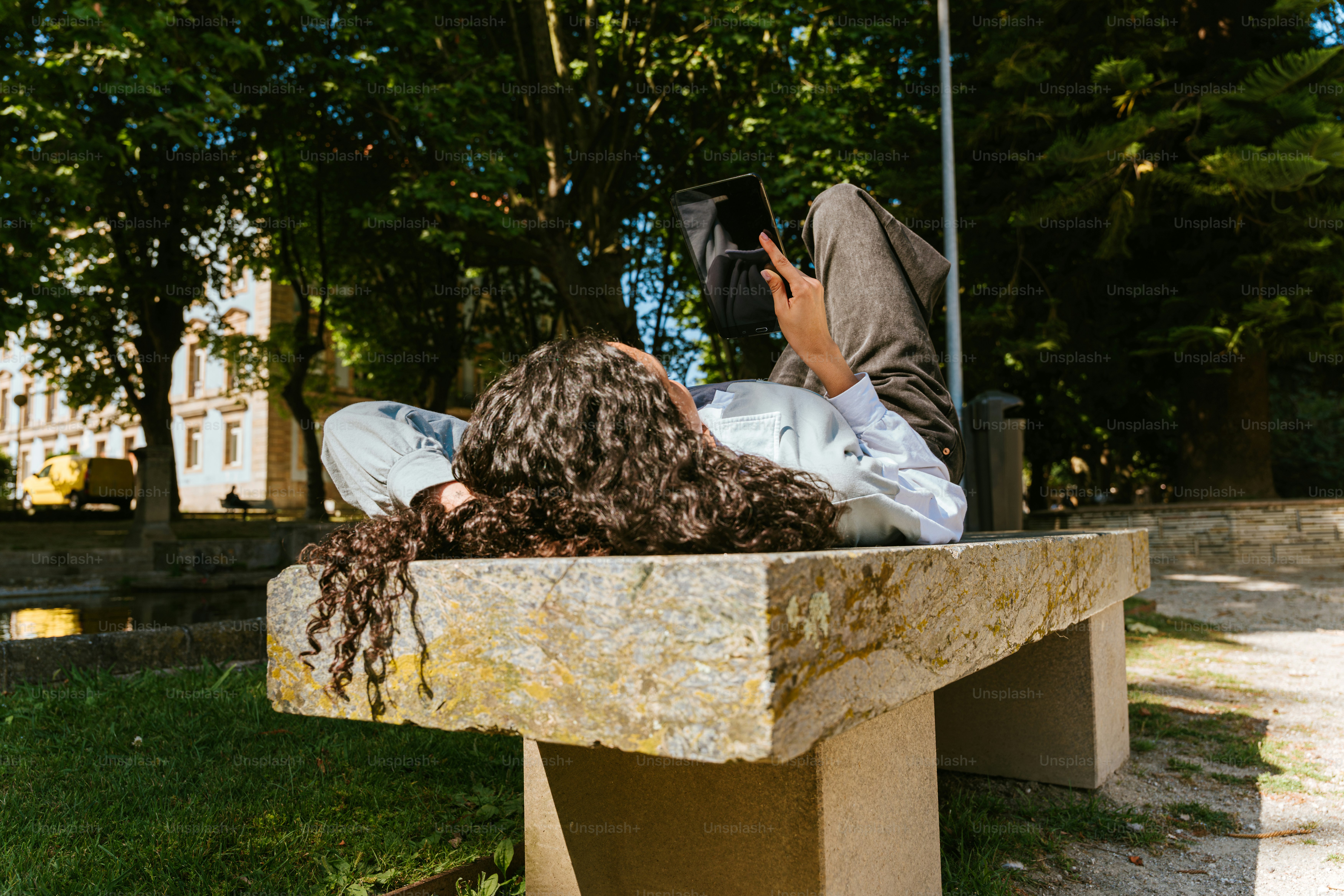 Person relaxing on a bench while using a tablet.