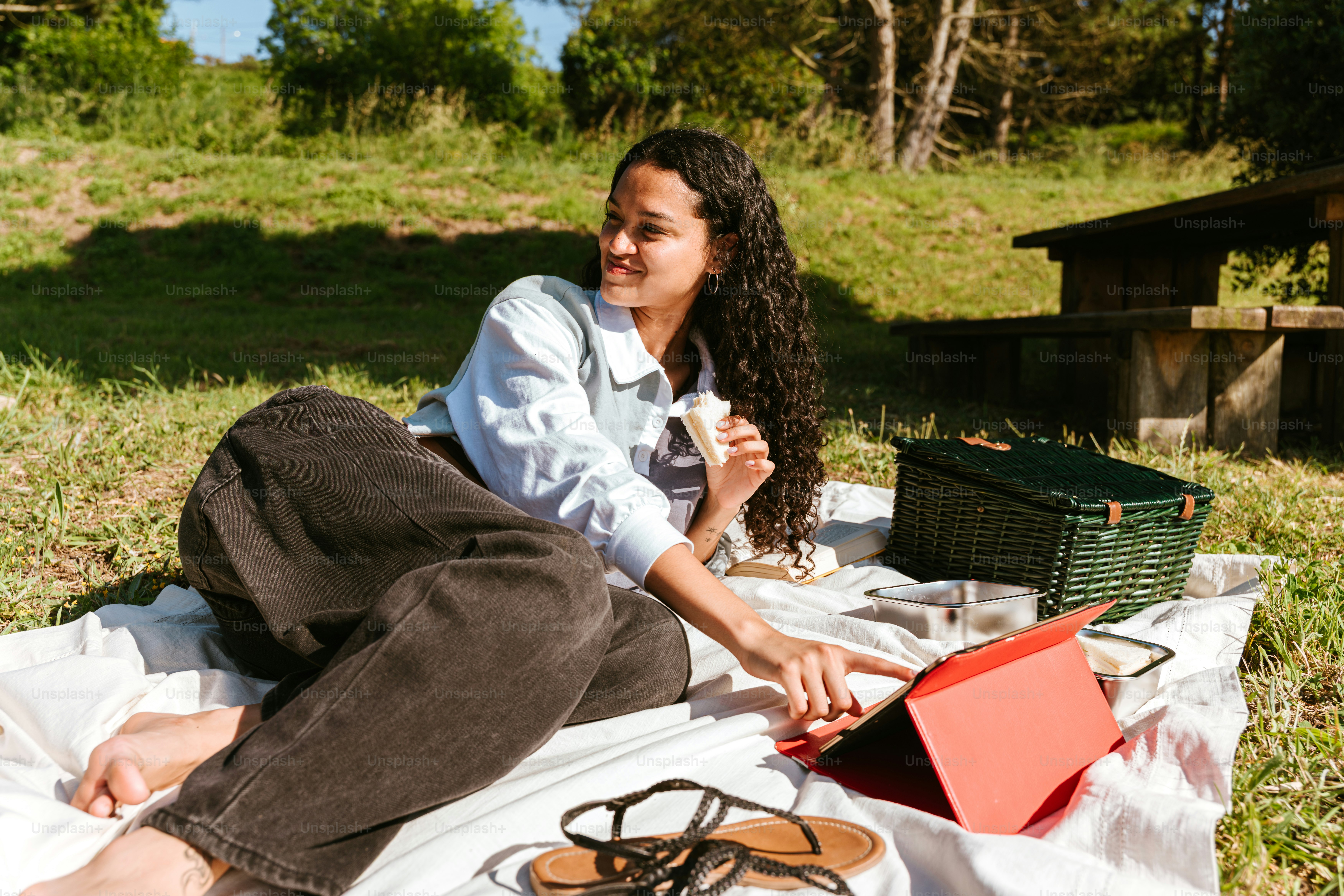Woman enjoys a picnic while using a tablet.