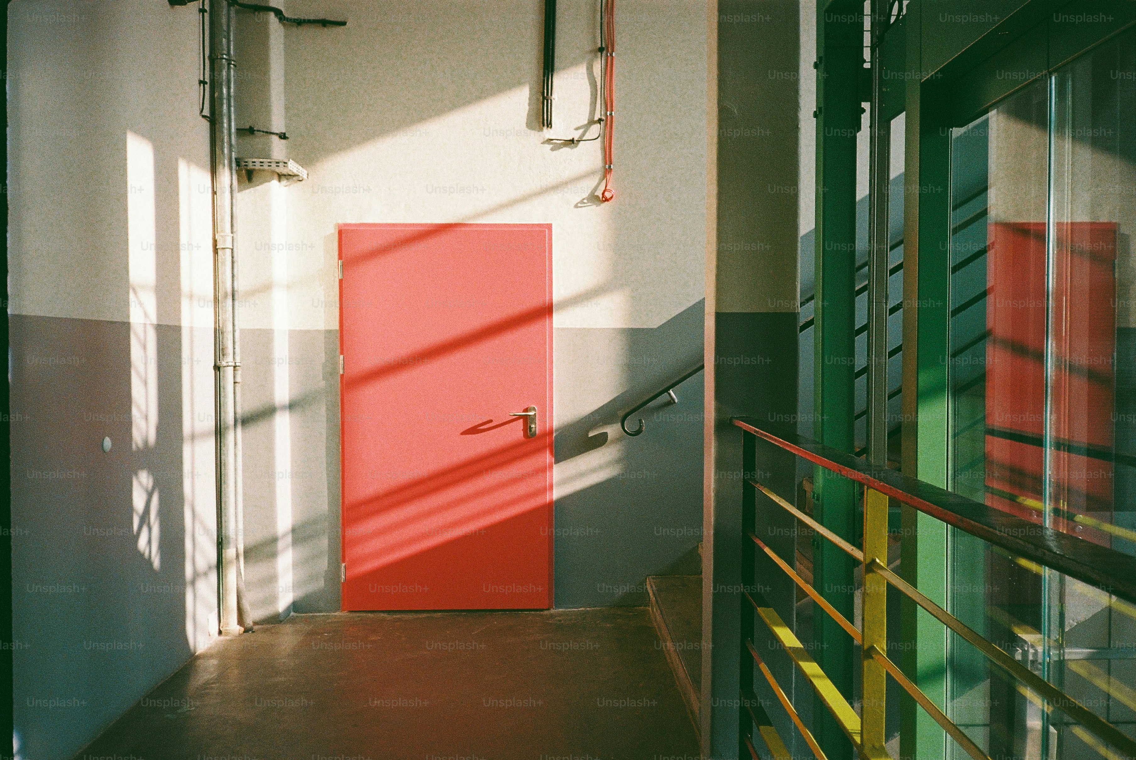 Une porte rouge projette des ombres dans un couloir.
