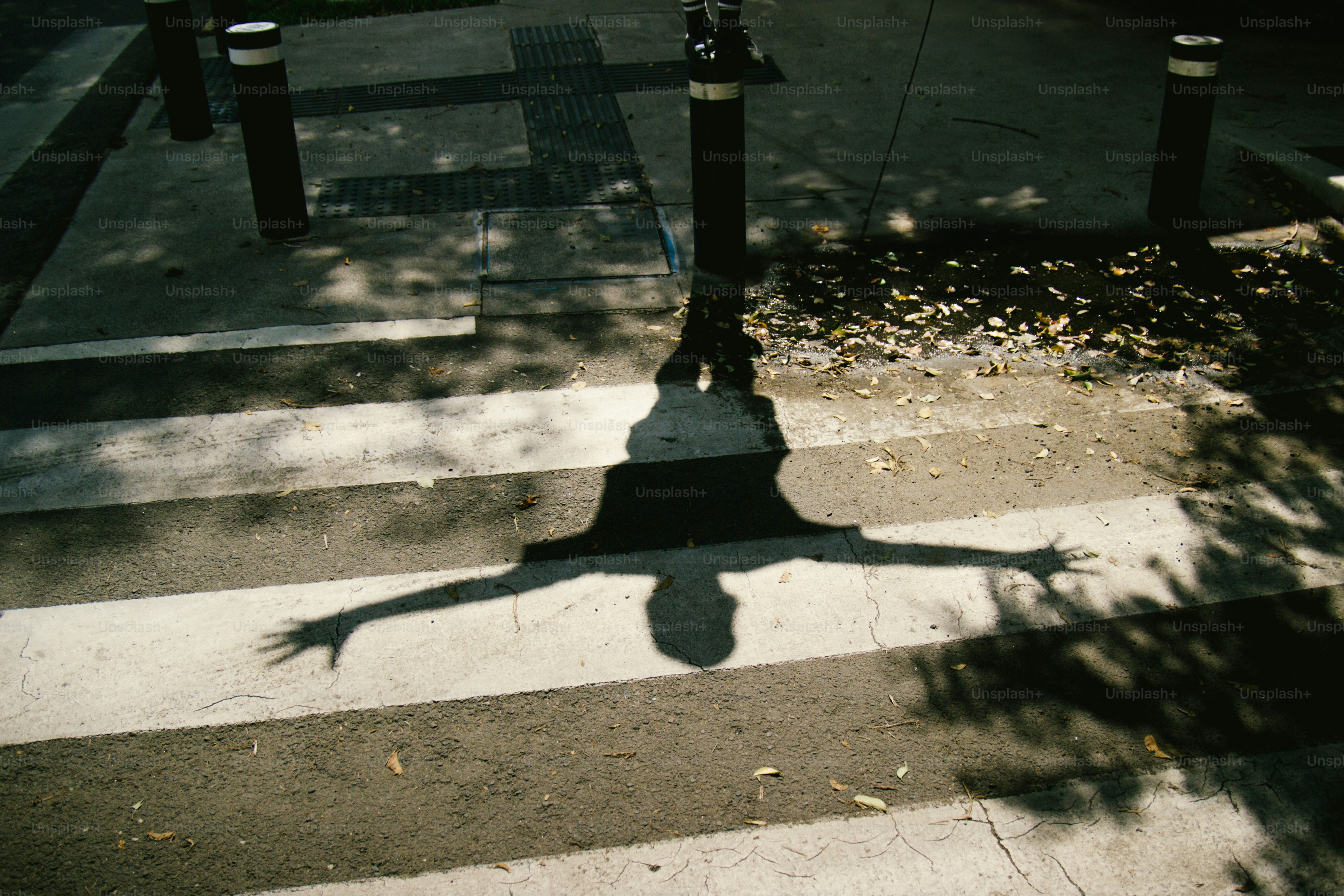A shadow with arms outstretched on a crosswalk.