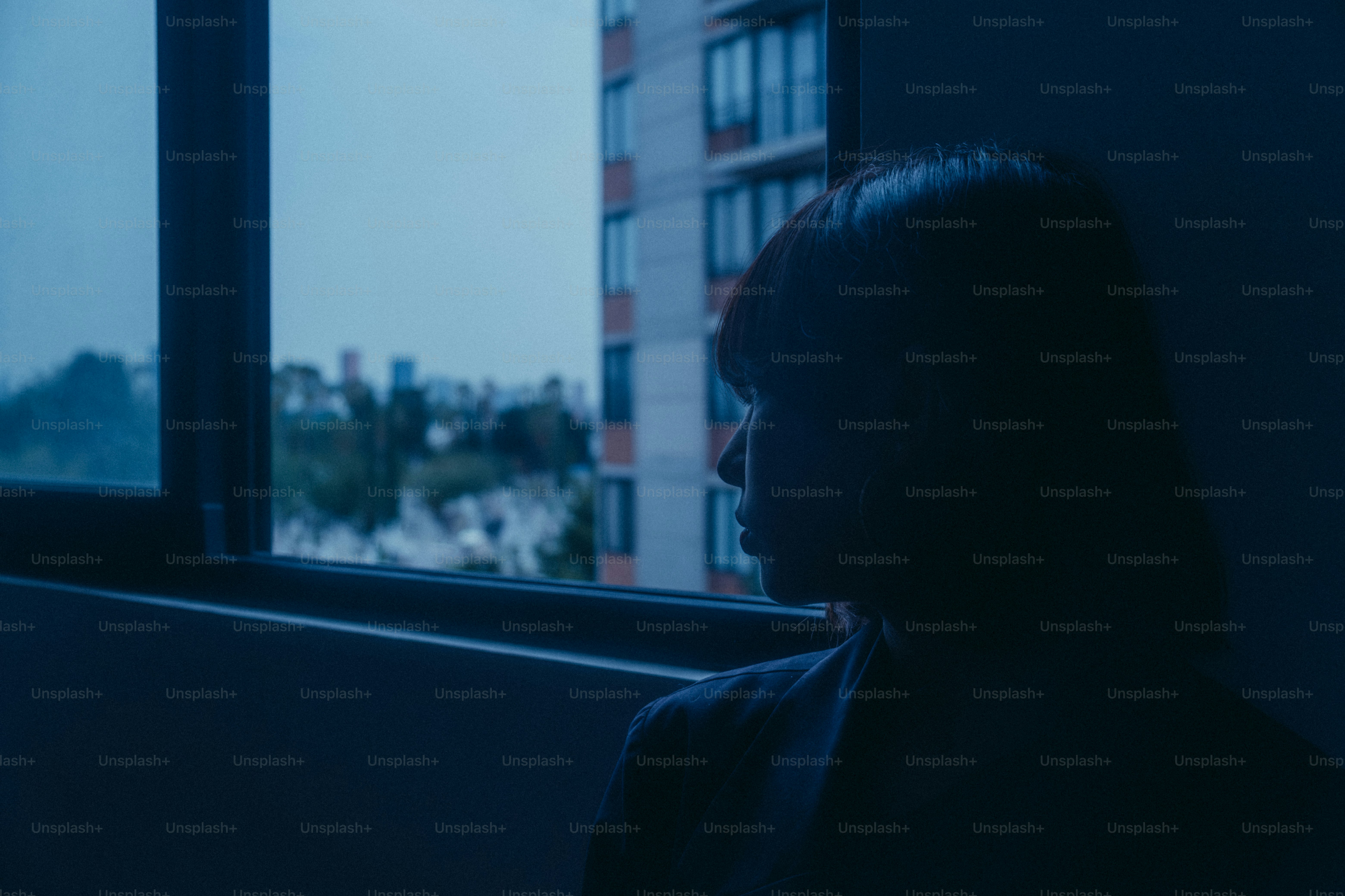 A woman looks out of a dark window.