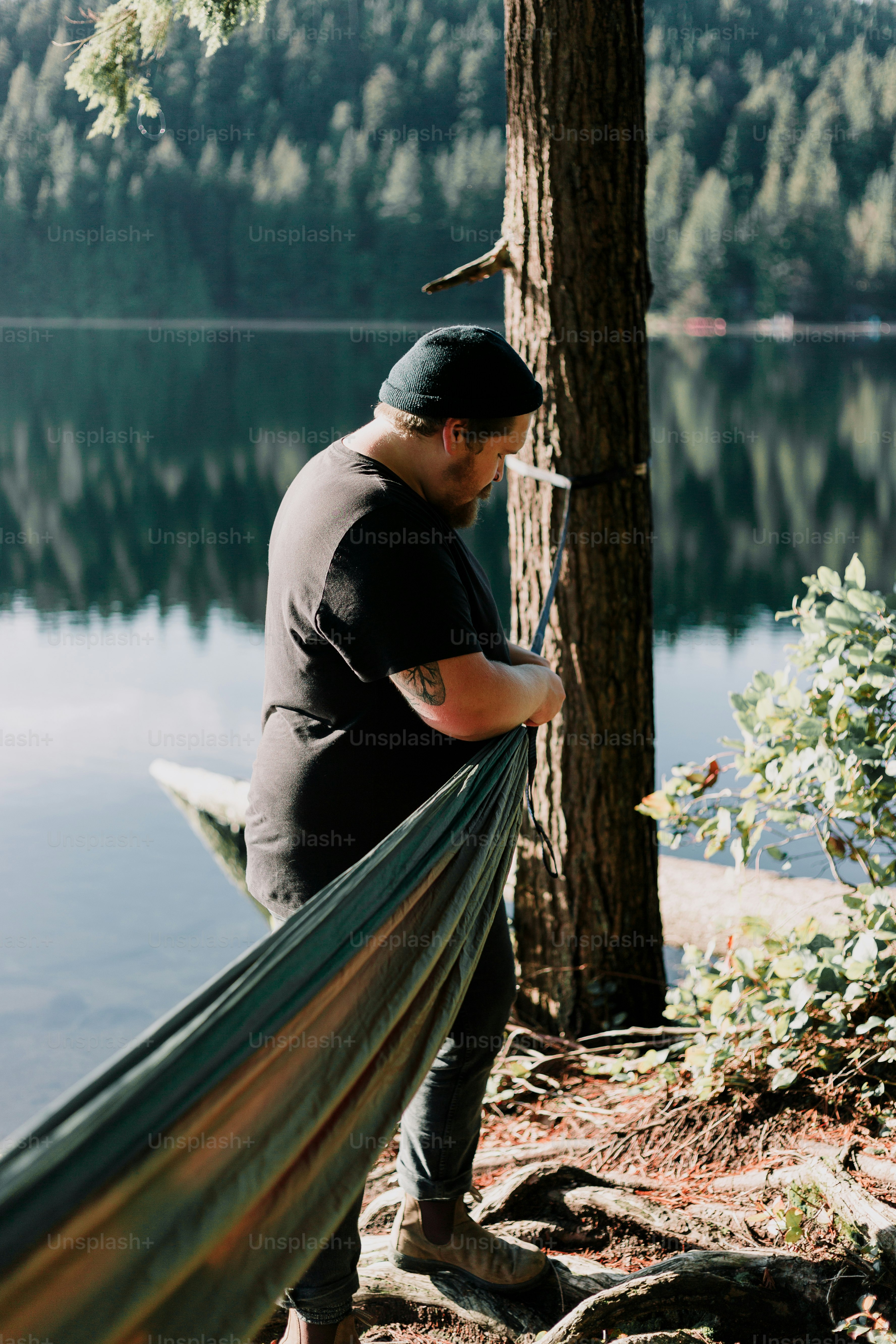 Man sets up a hammock by a serene lake.