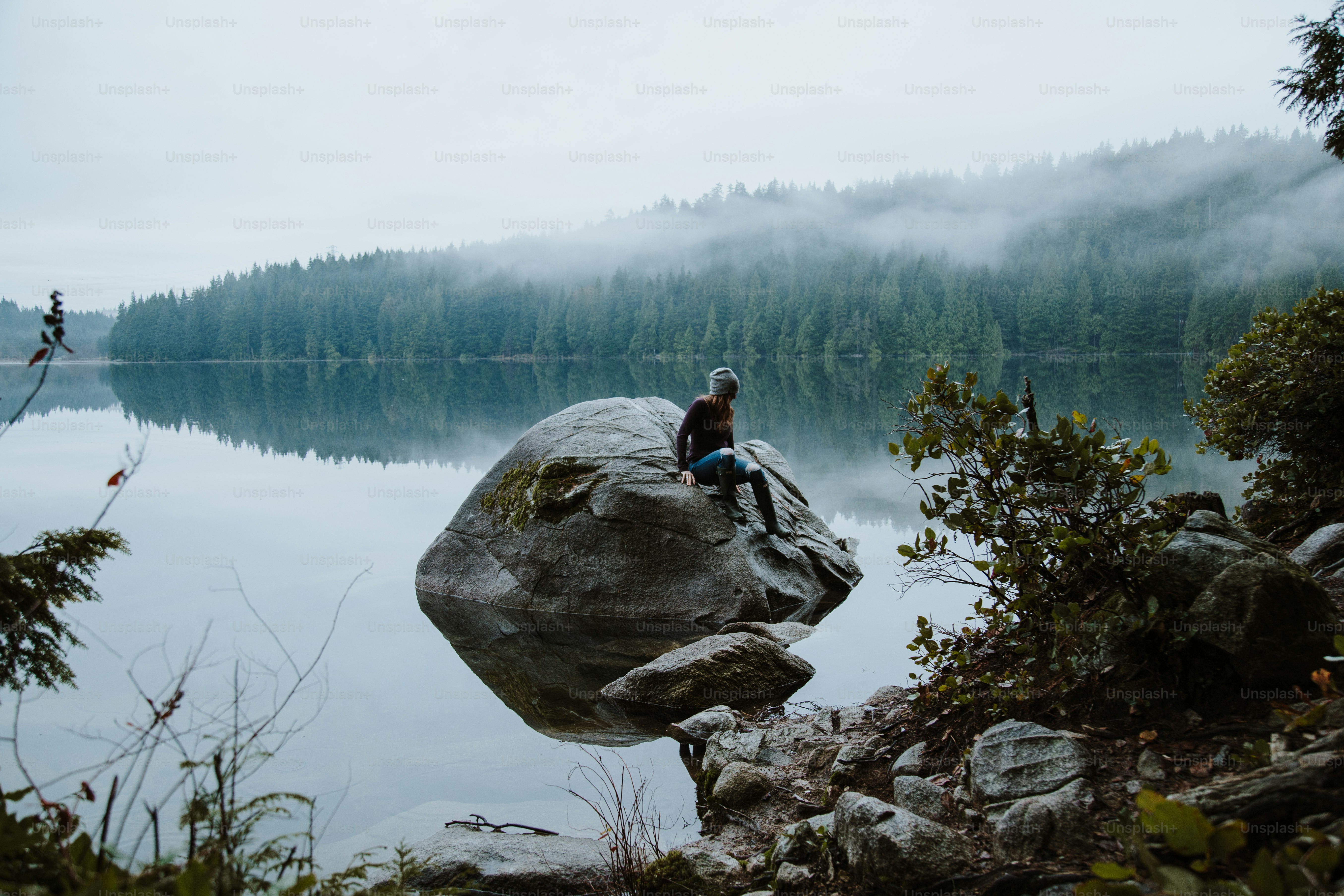 Person sits on a rock overlooking a serene lake.
